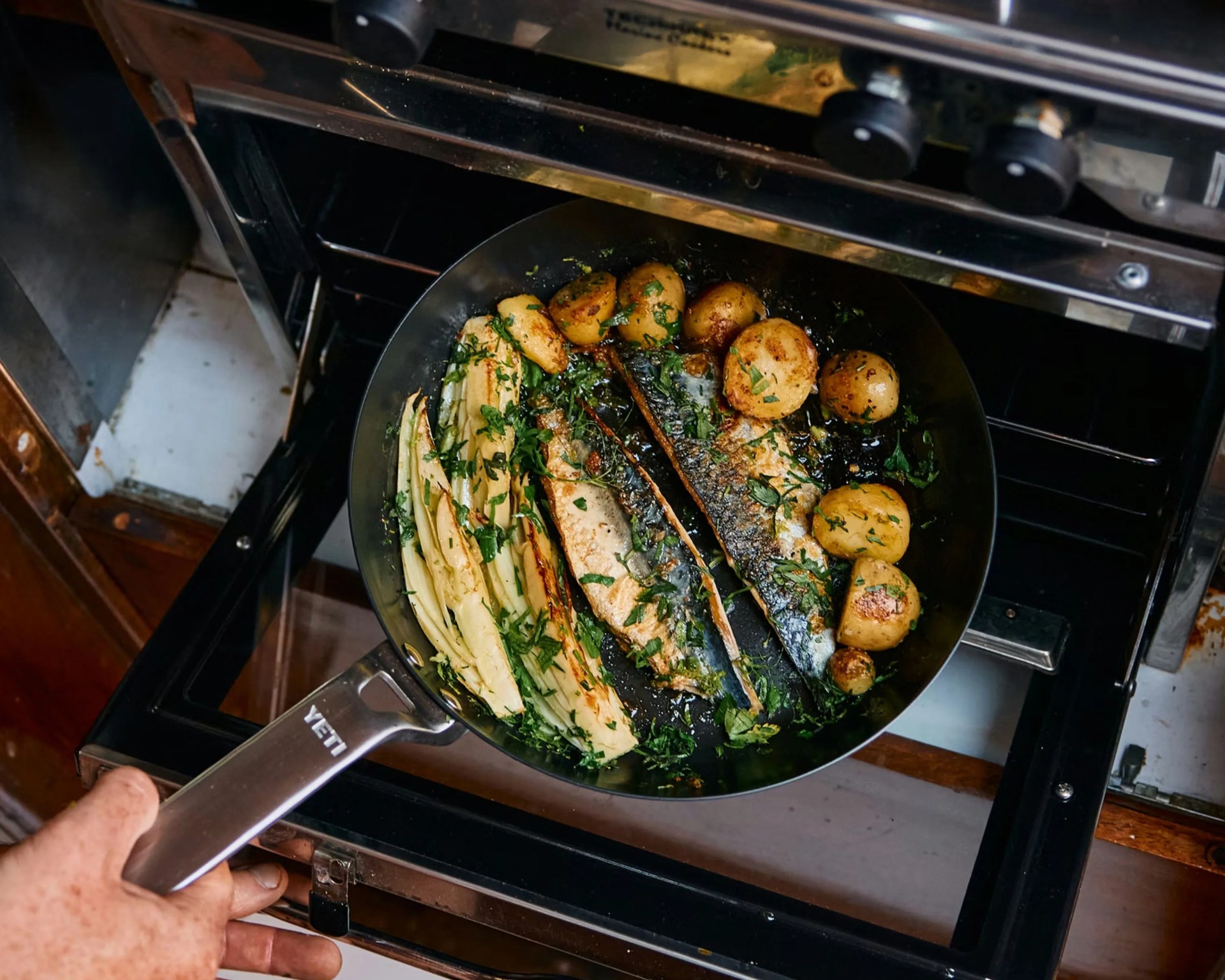 Black Yeti frying pan with cooked fish, potatoes, and greens being taken out of an oven.