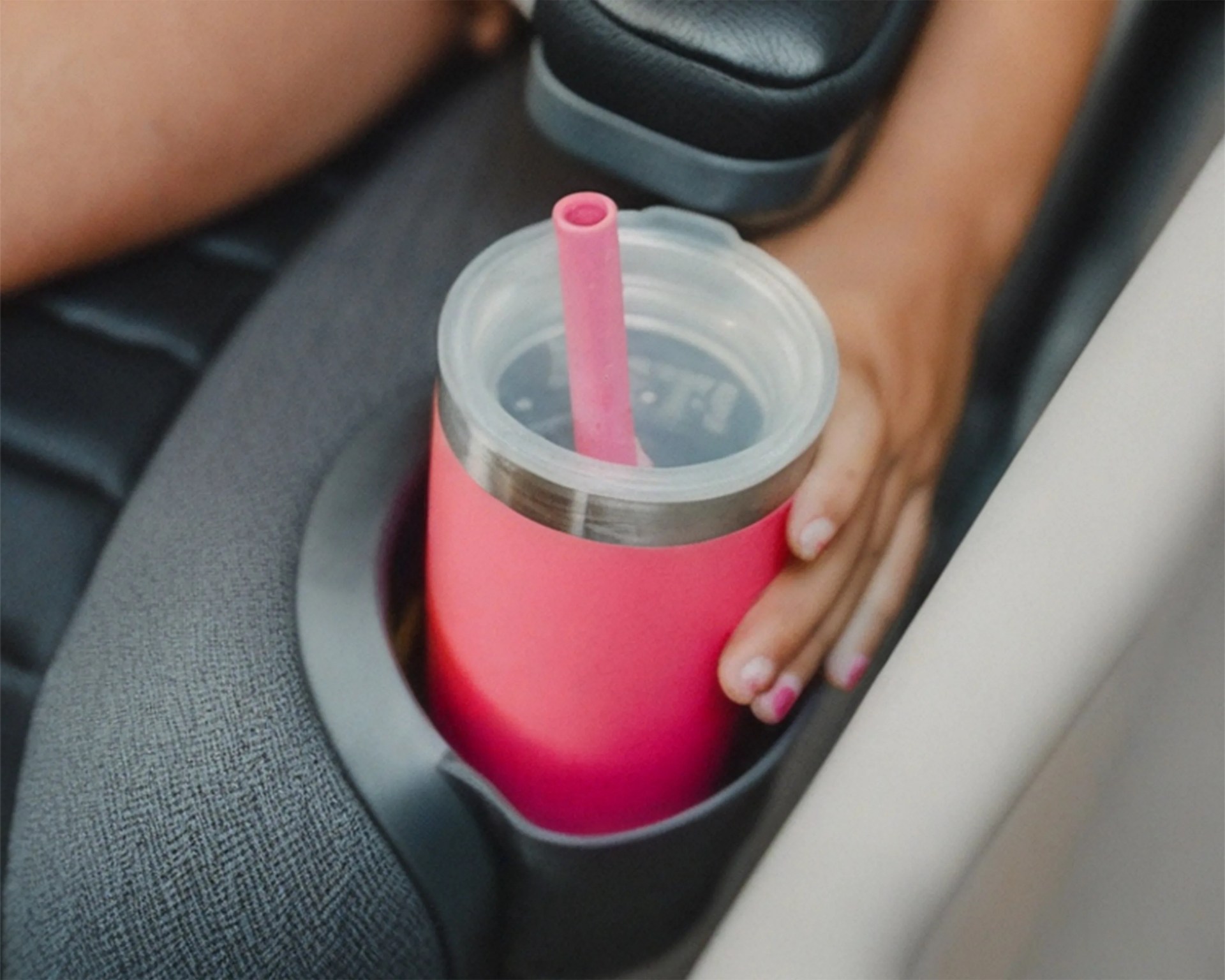 Pink insulated tumbler with a matching straw in a car cup holder held by a hand with pink nail polish.