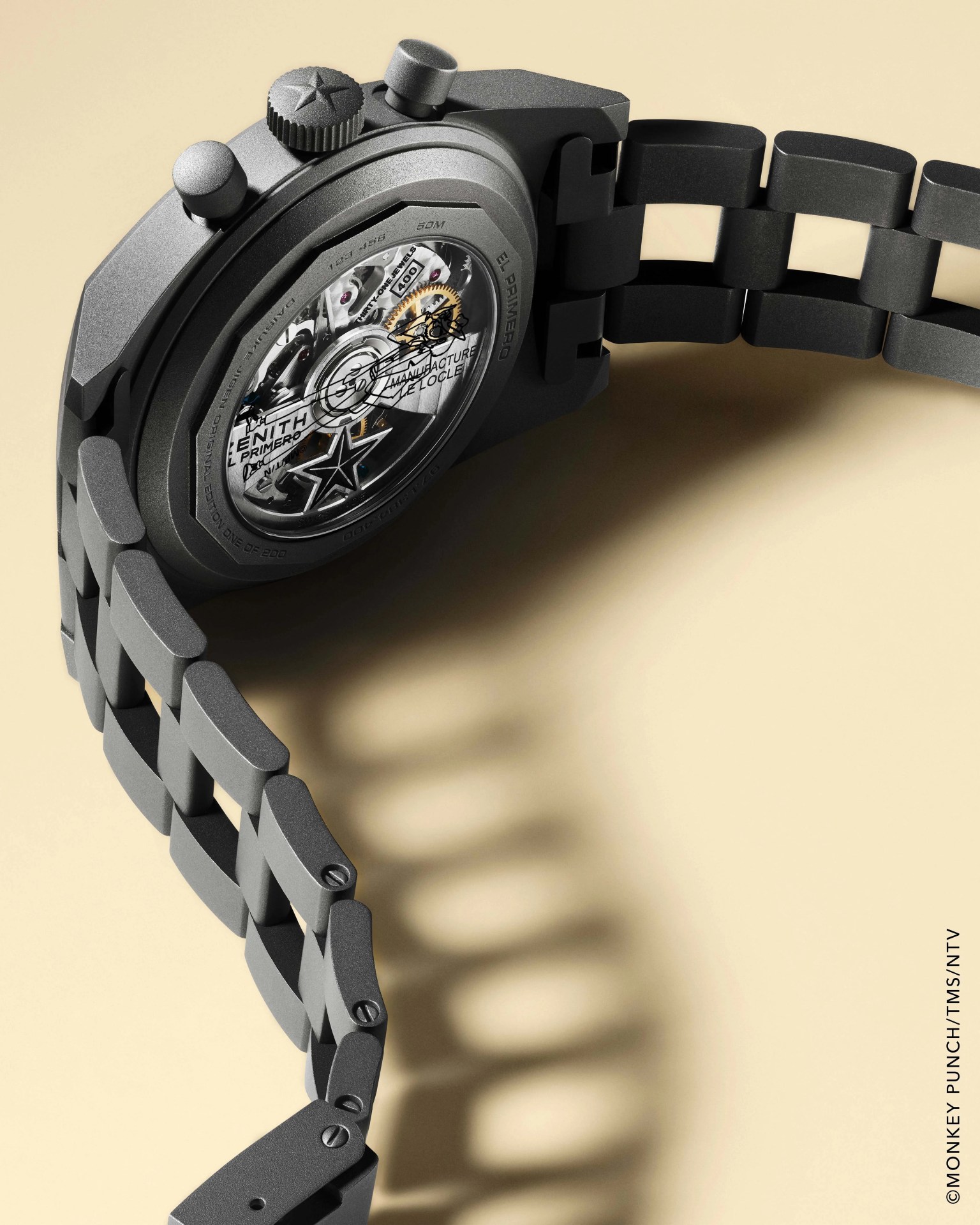 Matte black Zenith El Primero wristwatch with visible mechanical movement and linked metal bracelet on beige background.