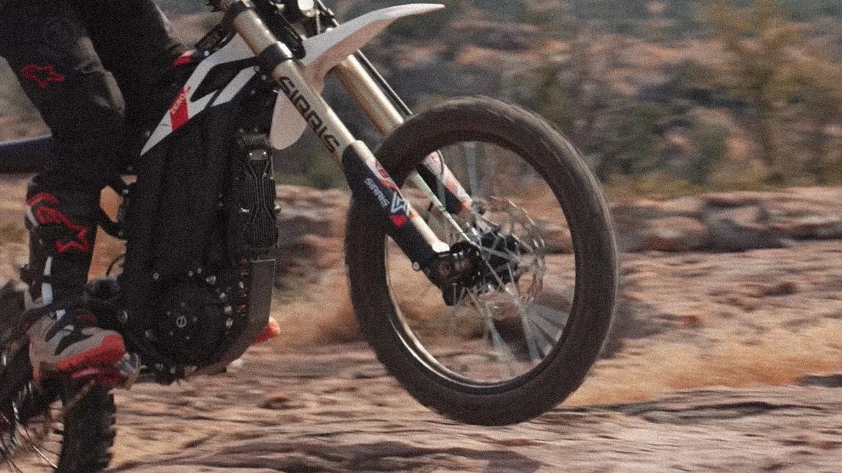 Front wheel and suspension fork of a dirt bike in mid-air over rocky terrain.