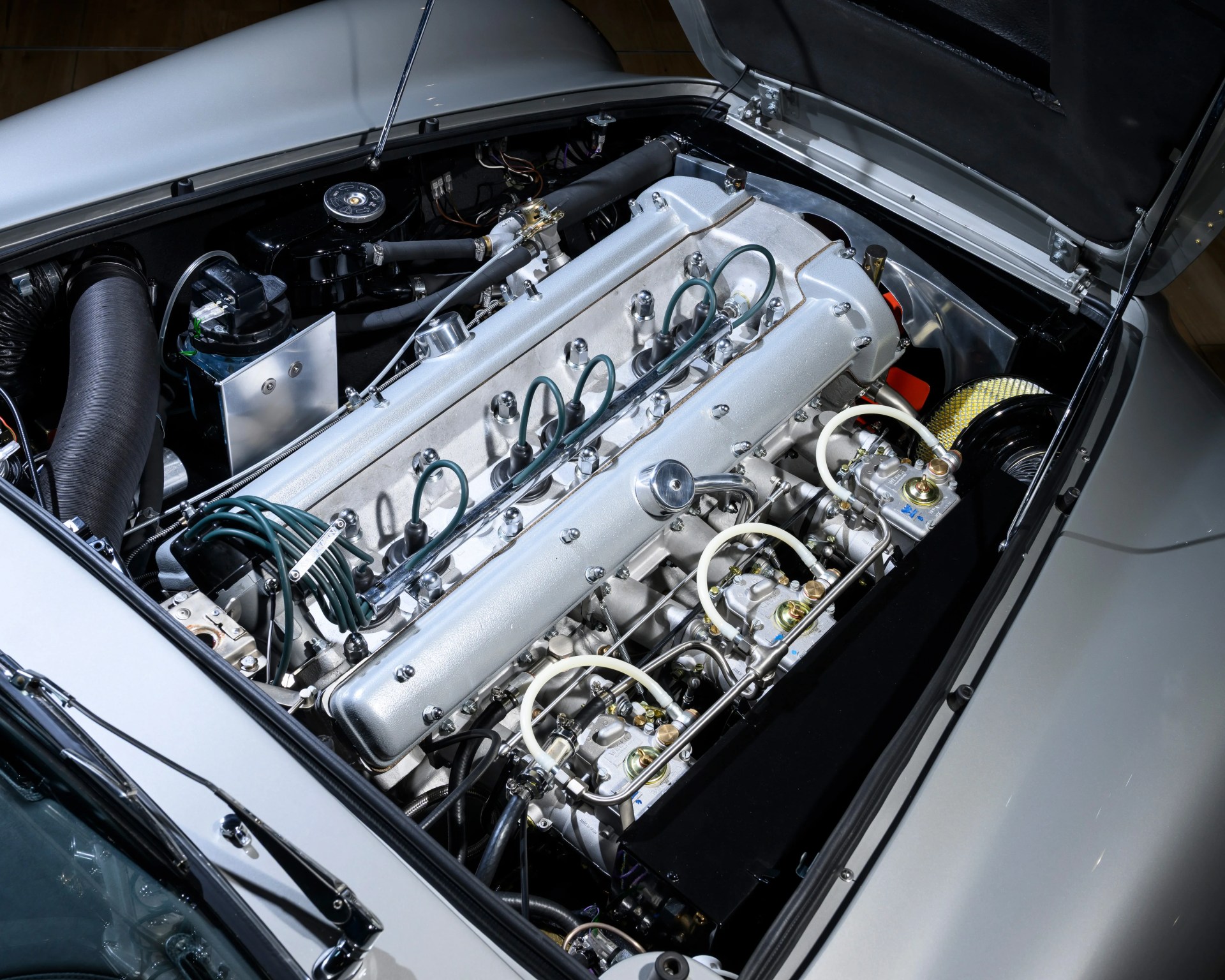 Silver inline six-cylinder engine with green ignition wires in a classic car engine bay.