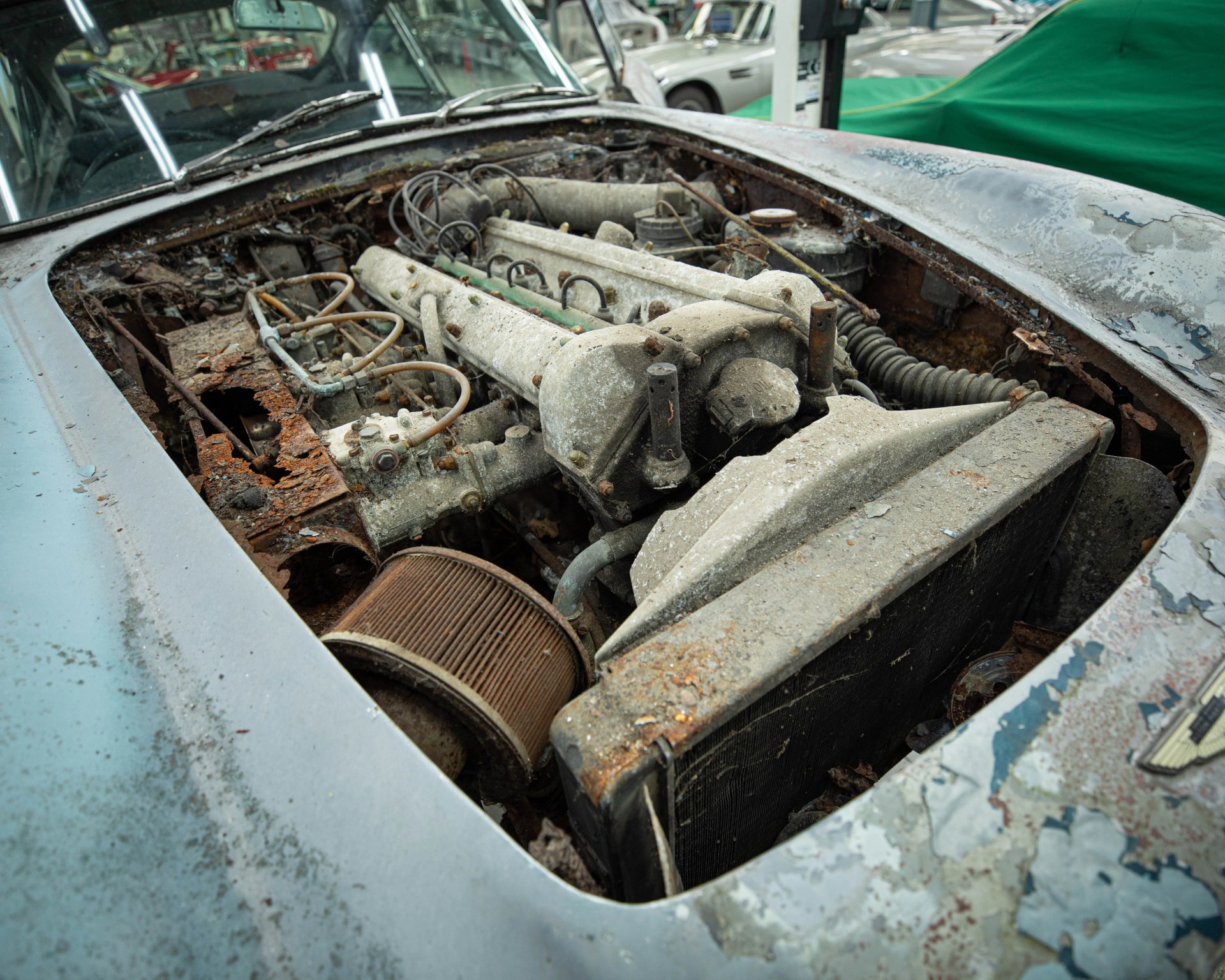 Rusty and dusty engine compartment of an old, weathered car with peeling paint on the hood.
