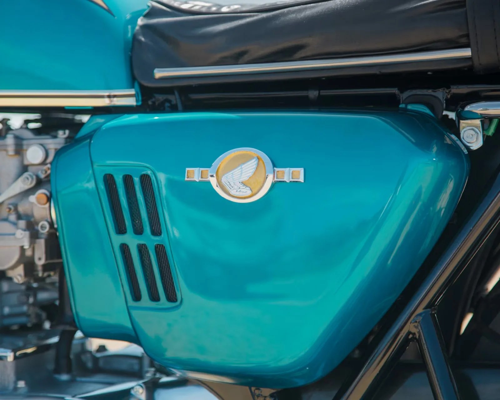 Teal motorcycle side cover with a silver wing emblem and black vent slats.
