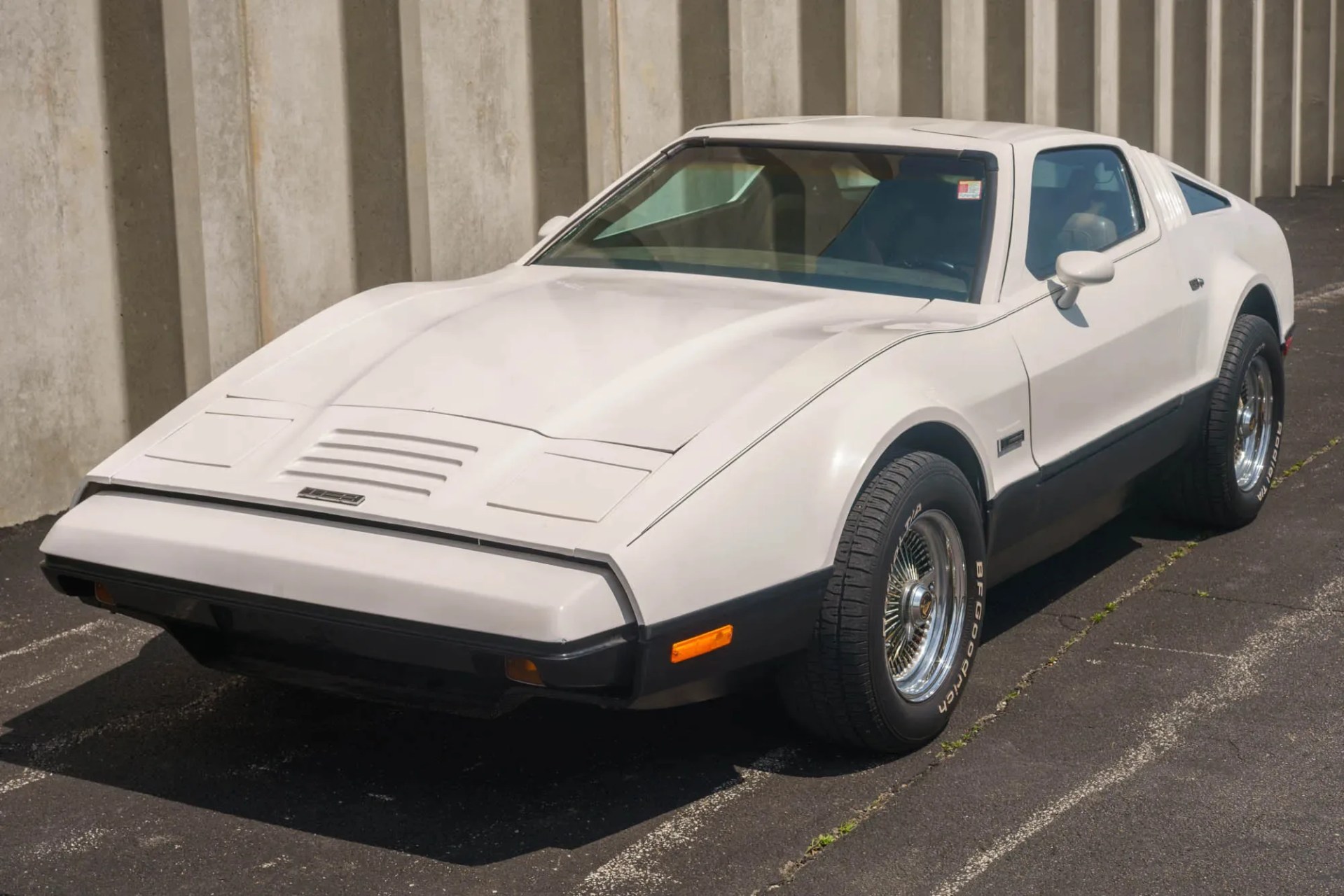 White vintage sports car with black lower trim and chrome wire-spoke wheels parked on asphalt.
