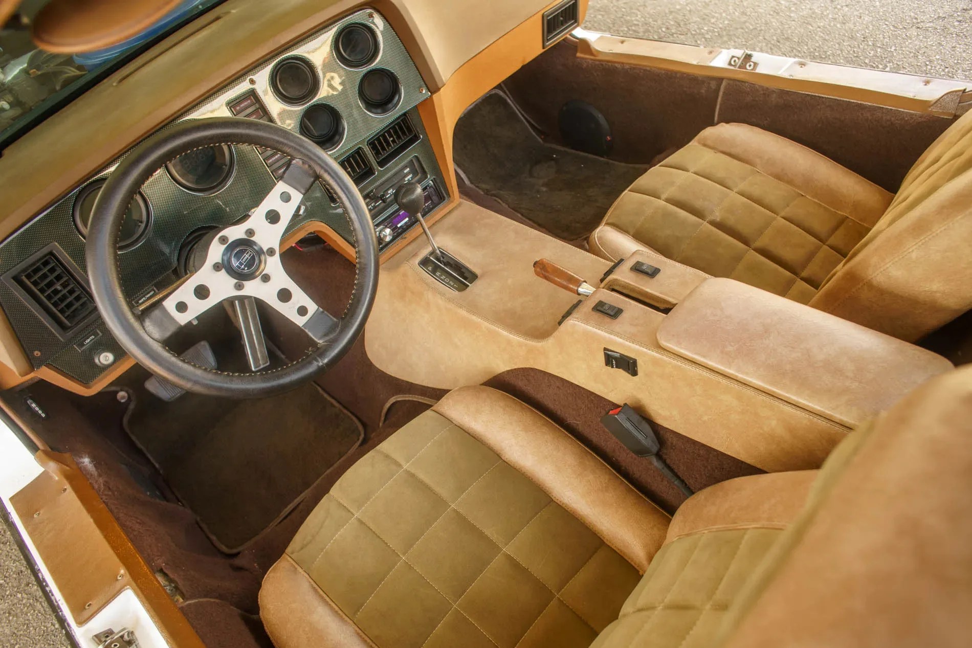 Vintage car interior with tan and olive green quilted seats, black steering wheel, and beige center console.
