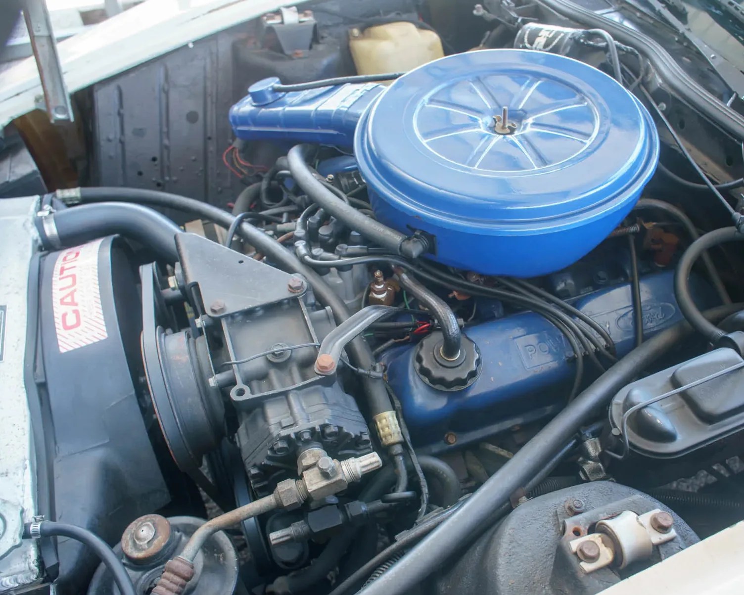 Blue engine with round air filter cover and various black hoses inside a car engine bay.
