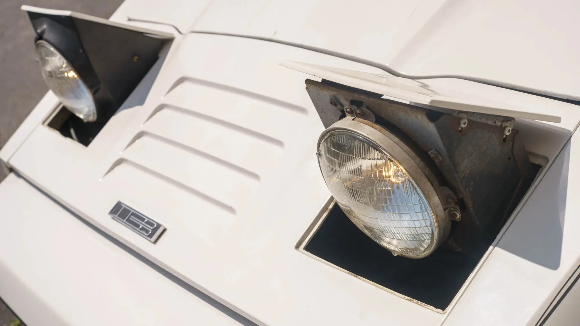 Close-up of white car front with raised pop-up headlights and a "T13" badge on the hood.