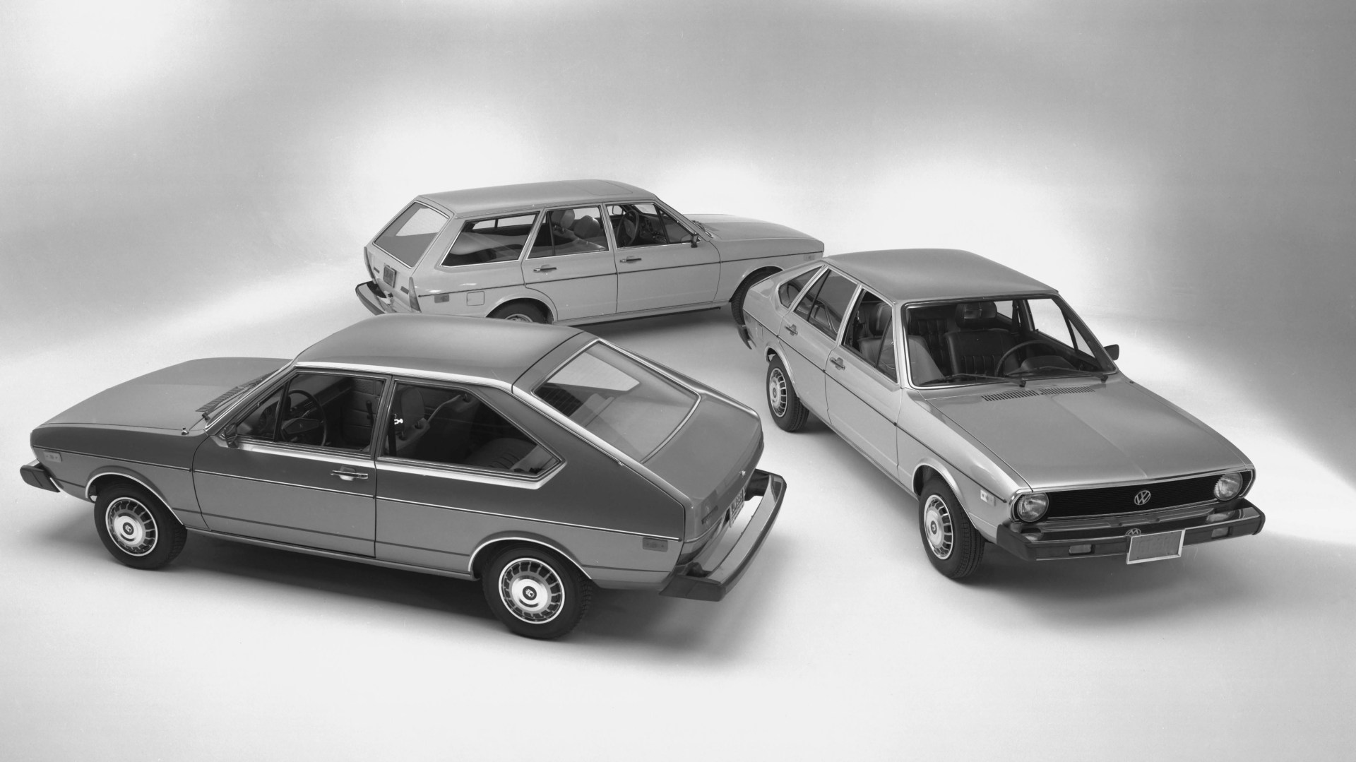 Three vintage Volkswagen cars in a studio setting, including a hatchback, a wagon, and a sedan, all in grayscale.
