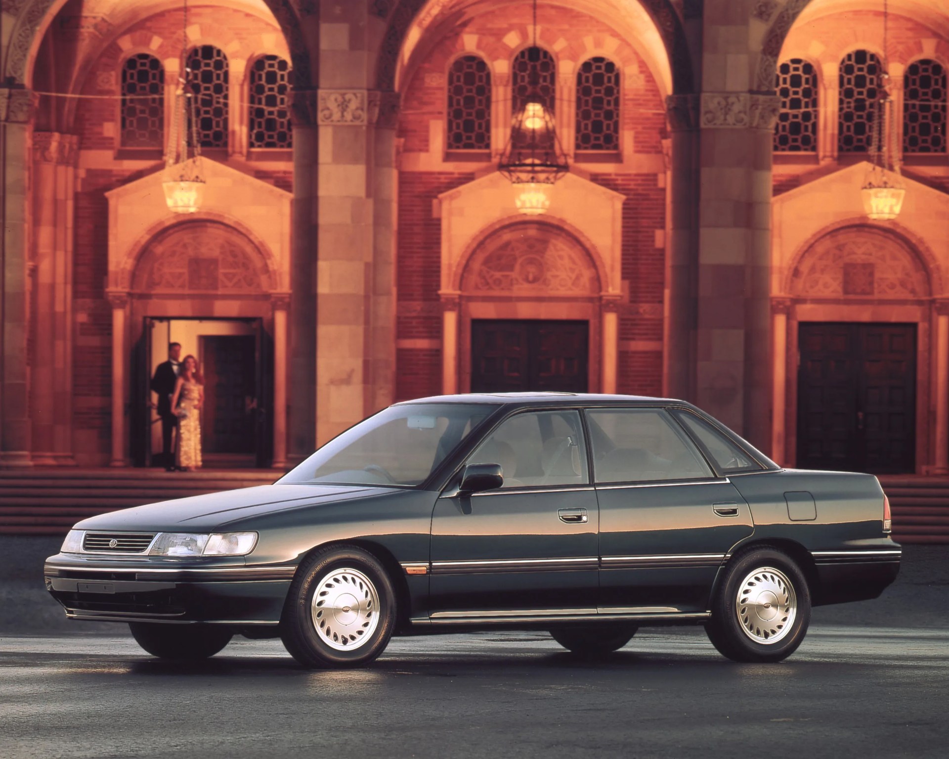 Dark green four-door sedan parked in front of a building with arched doorways and warm lighting.