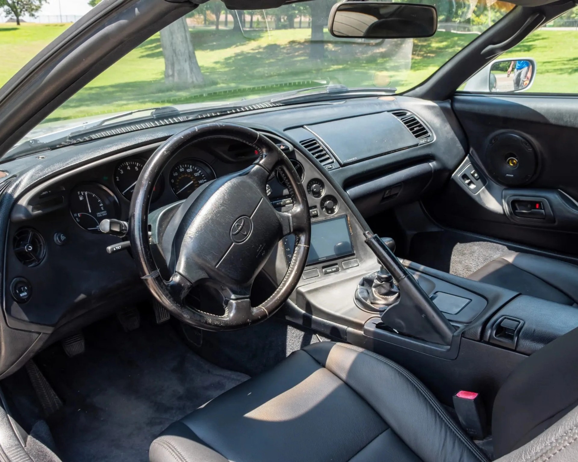 Black leather interior of a car featuring a three-spoke steering wheel with a Toyota logo, manual gear shift, and center console.