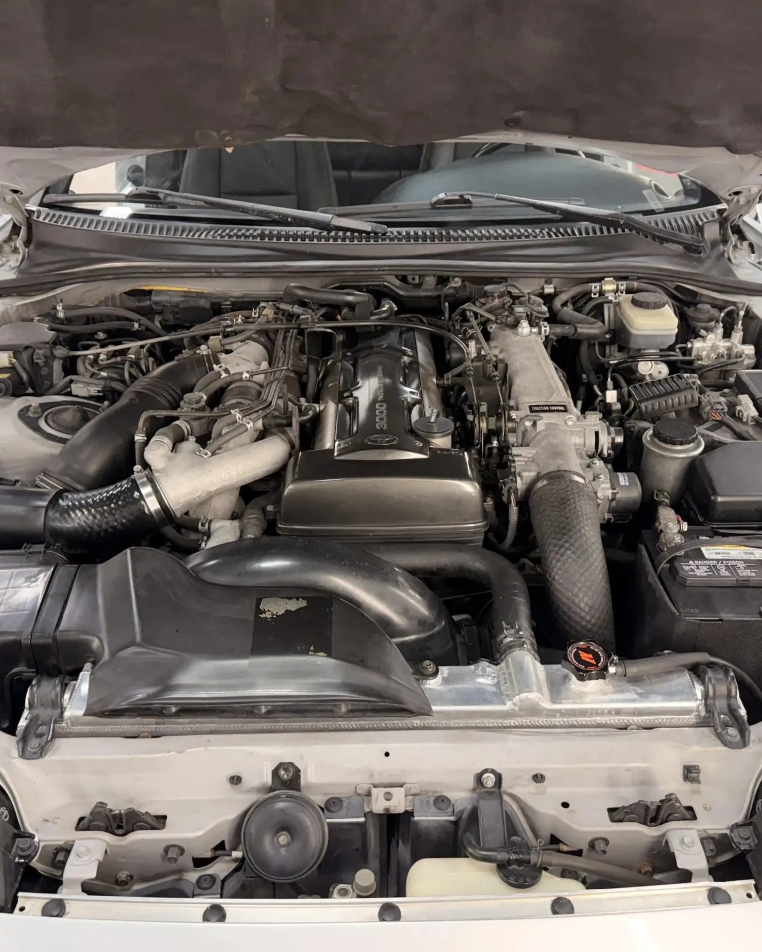 Car engine bay with a black valve cover labeled "3000" and various hoses and components visible.