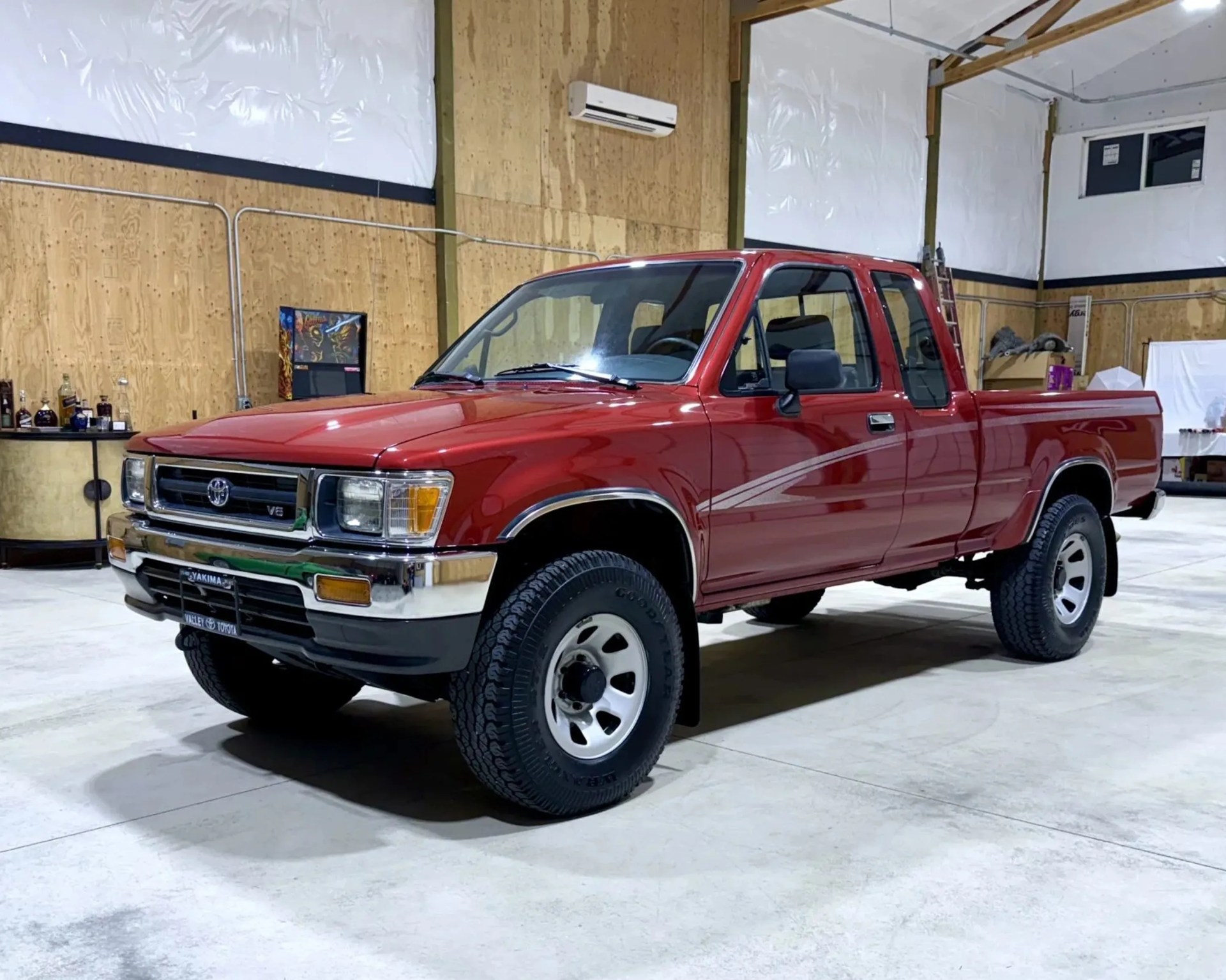 Red Toyota pickup truck with extended cab and V6 badge parked indoors on a concrete floor.