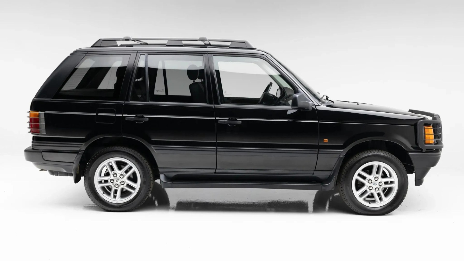 Black classic Range Rover SUV with silver alloy wheels and roof rails in a studio setting.