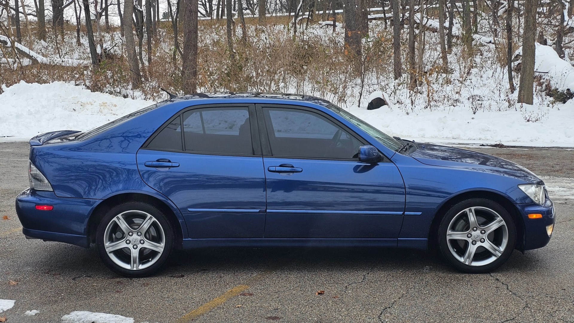 Blue four-door sedan with tinted windows parked on a snowy roadside.
