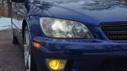 Front left side of a blue car showing the headlight, amber side marker, and yellow fog light.