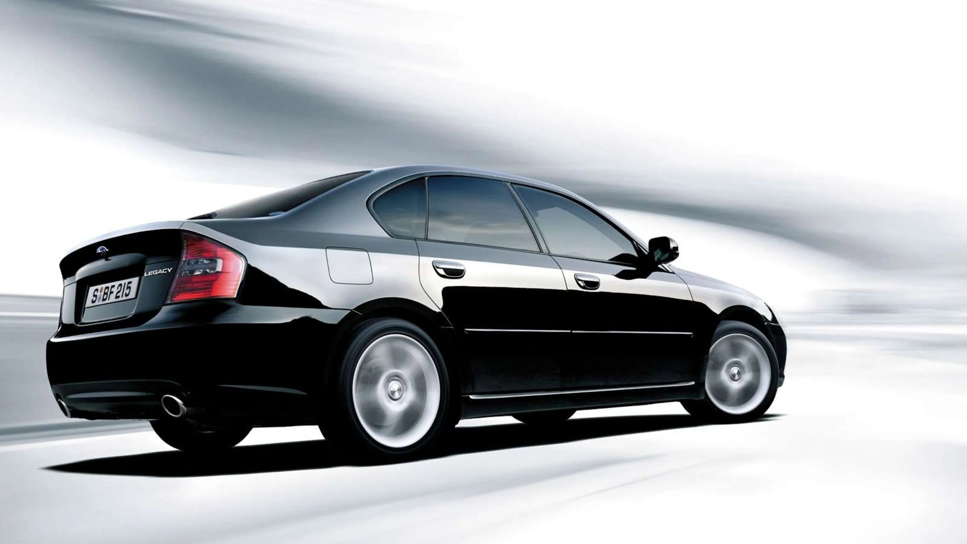 Black Subaru Legacy sedan with tinted windows driving on a blurred white and gray background.