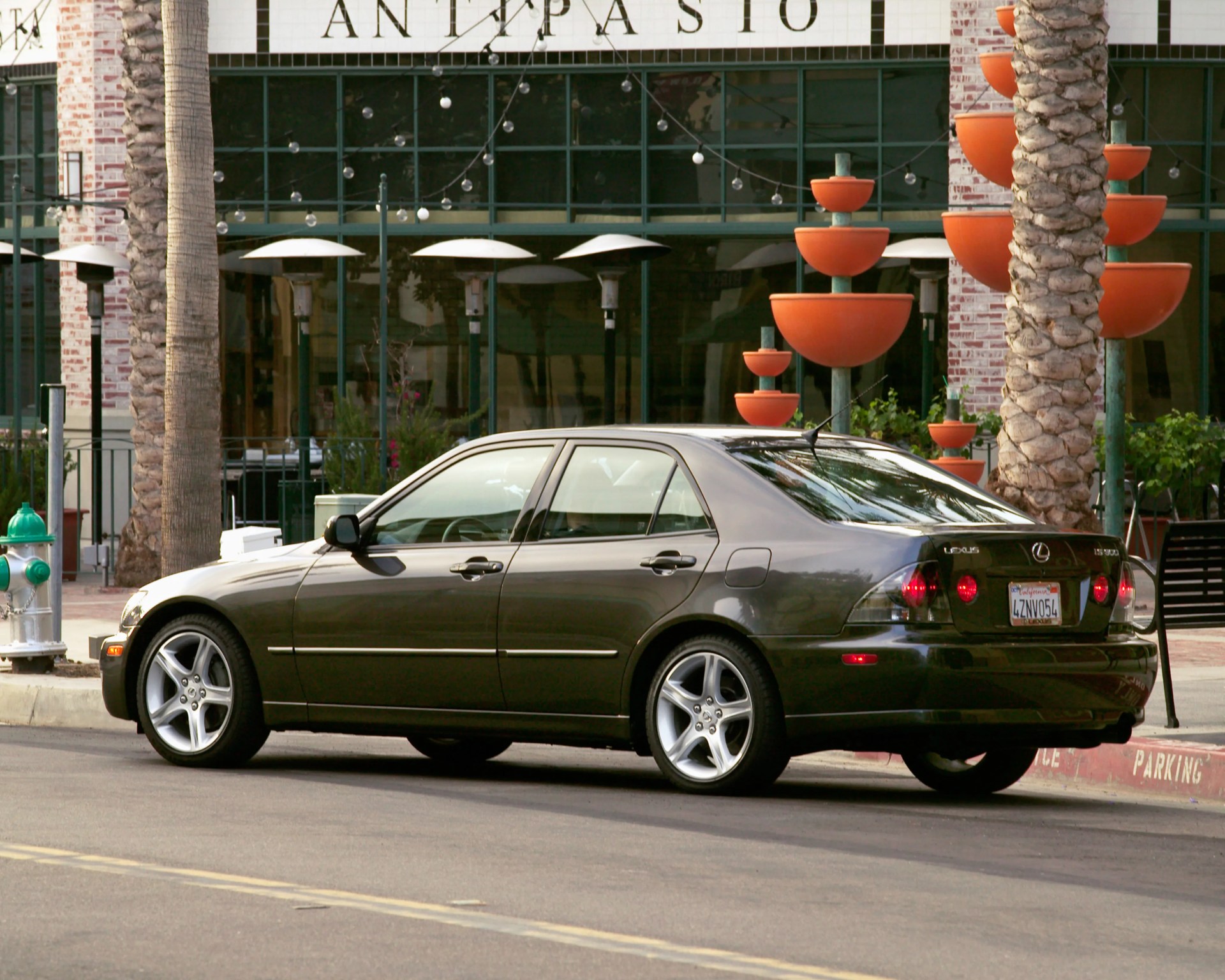 Dark gray Lexus IS 300 sedan parked on a street in front of a building with orange tiered planters and palm trees.