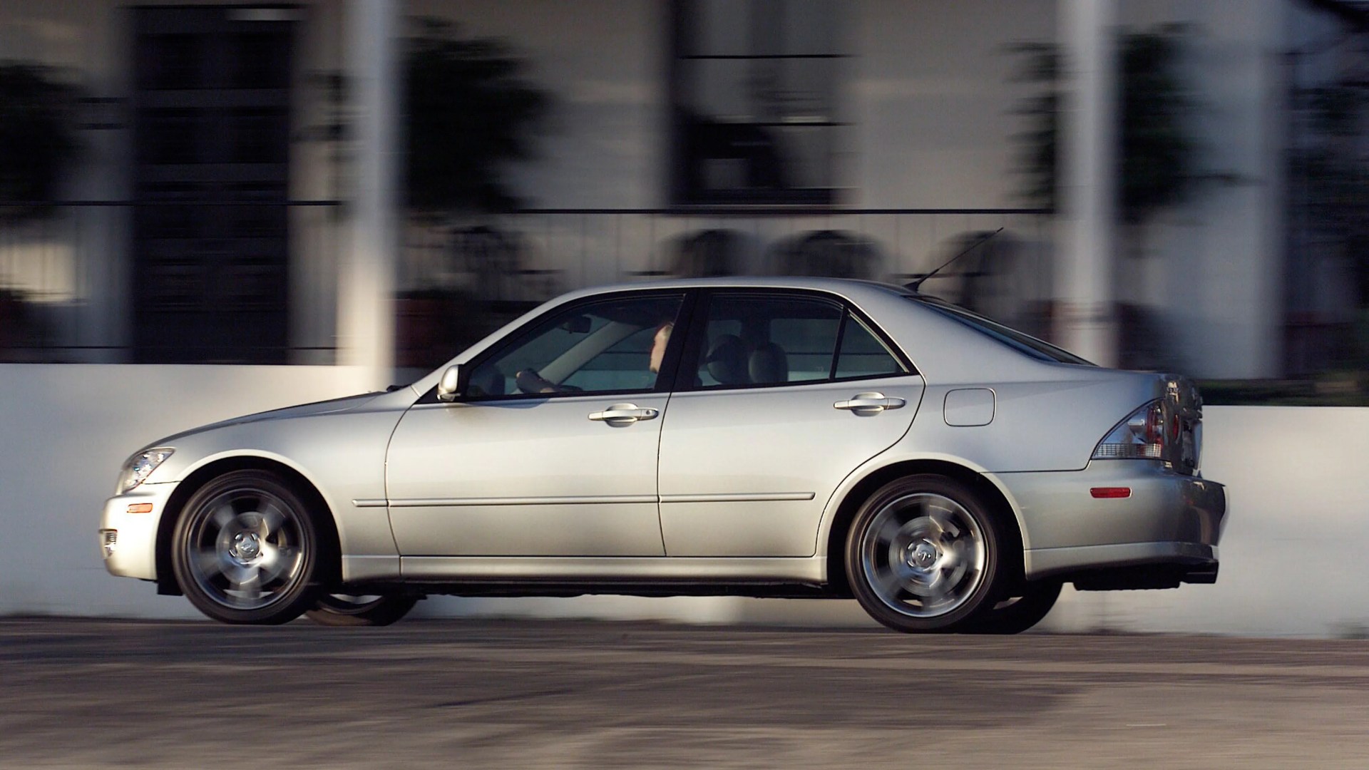 Silver four-door sedan driving on a paved road with motion blur on the wheels.