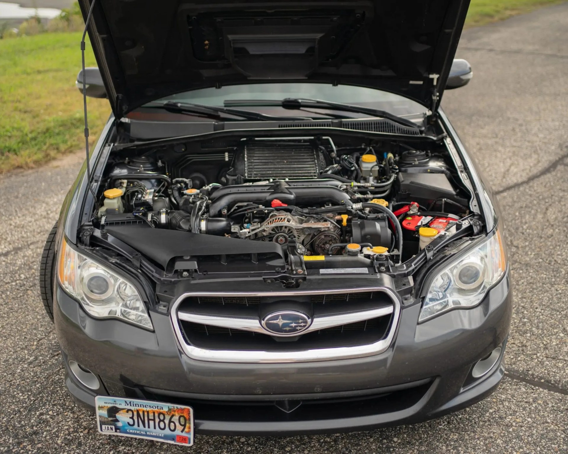 Front view of a gray Subaru car with the hood open, showing the engine and a Minnesota license plate.