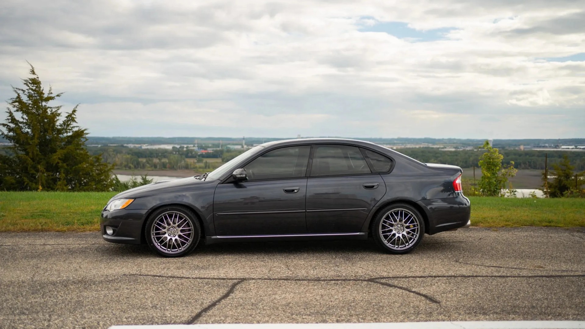 Dark gray sedan with tinted windows and multi-spoke alloy wheels parked on asphalt near grass.