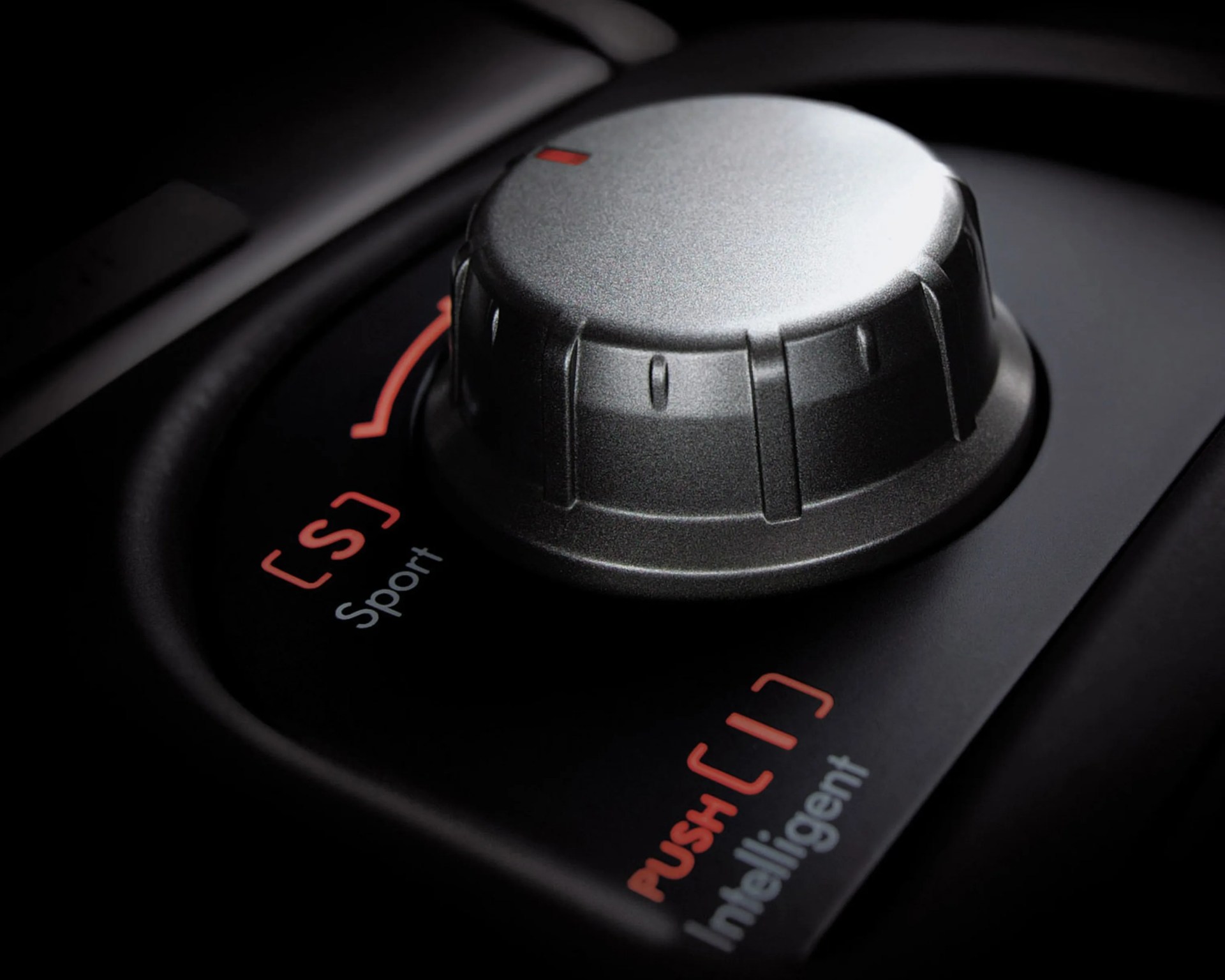 Close-up of a metallic car control knob with settings labeled "Sport" and "Intelligent" in a black console.