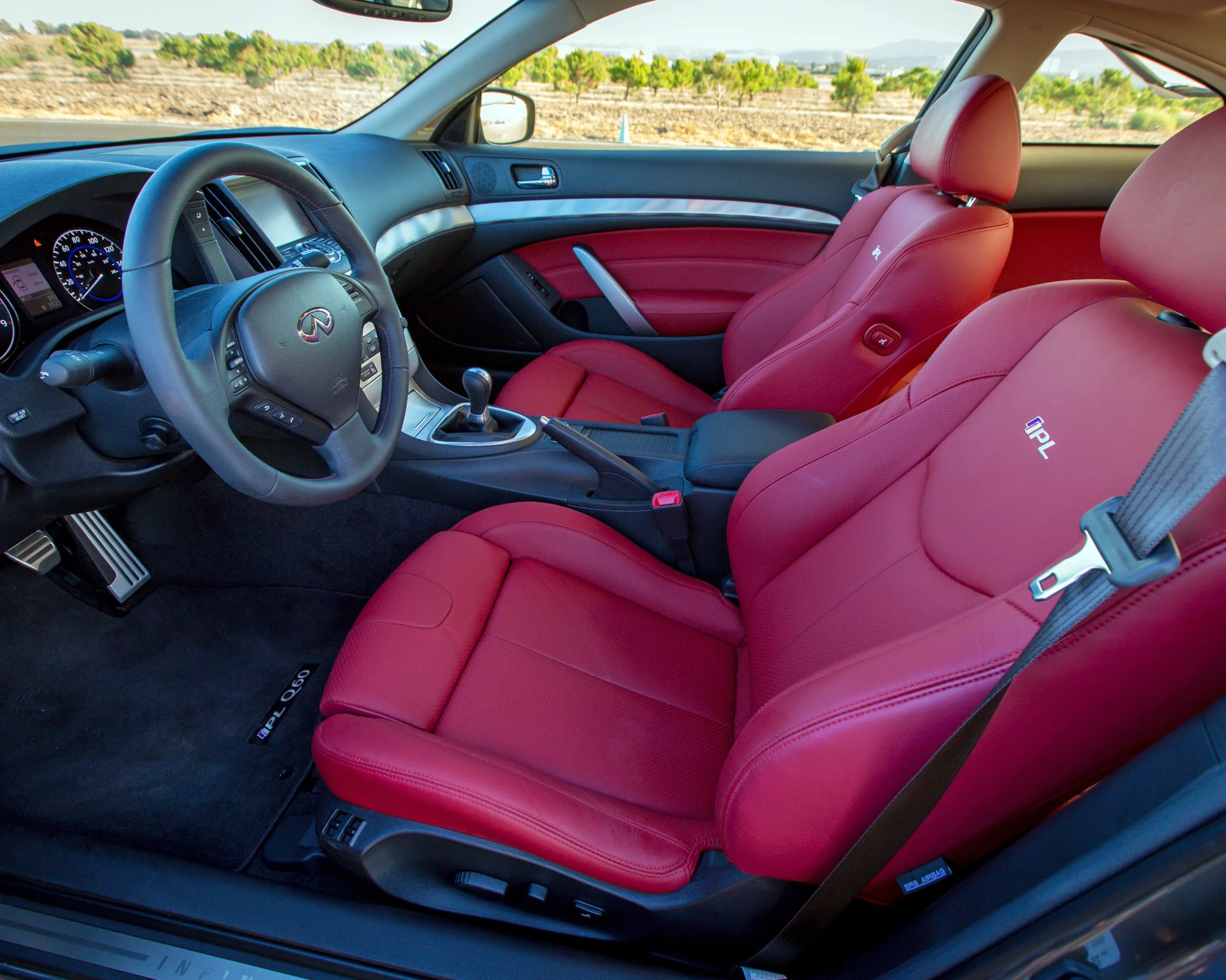 Car interior with red leather IPL sport seats, black steering wheel with Infiniti logo, and manual gear shift.