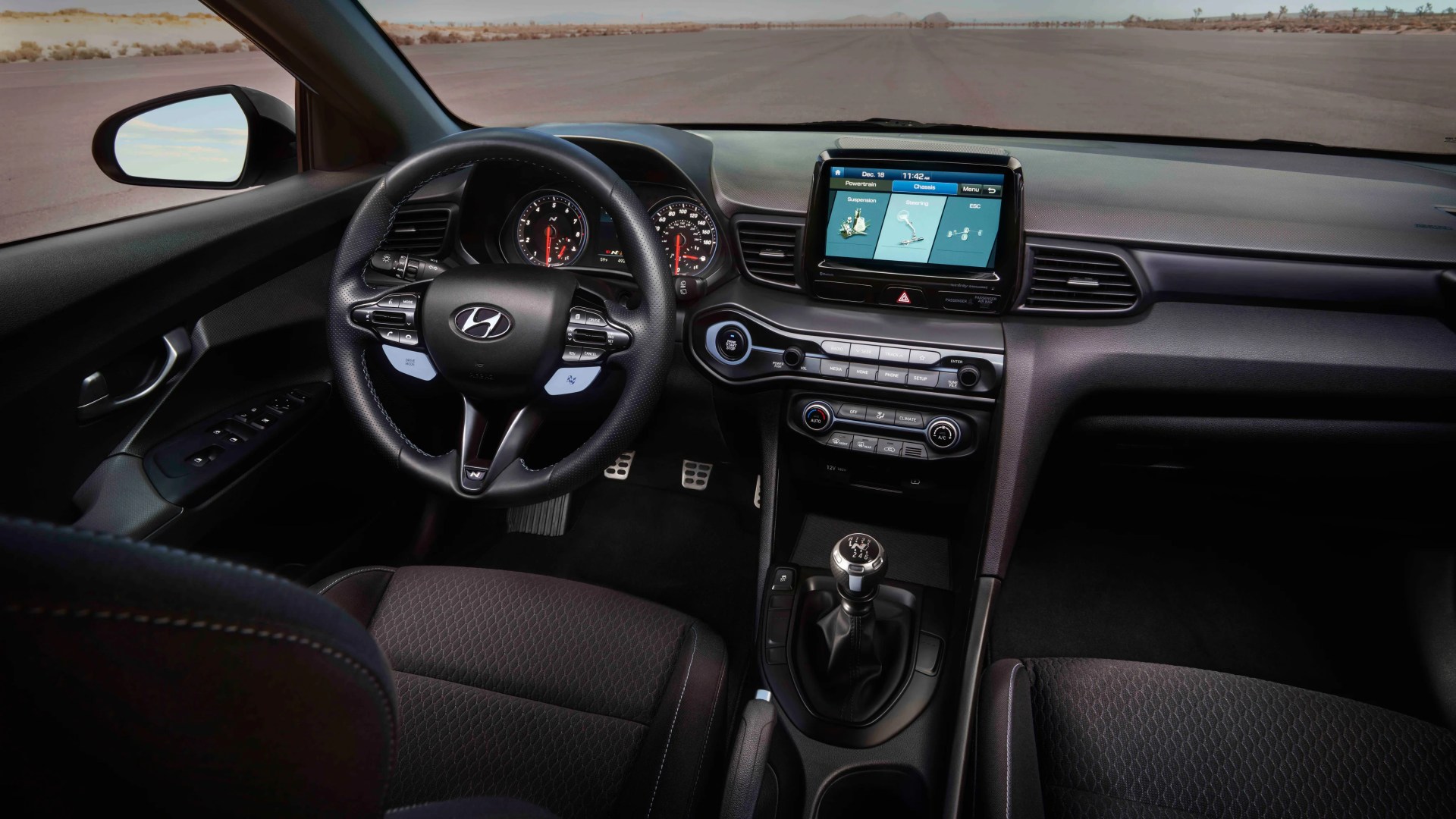 Interior view of a Hyundai car showing a black leather steering wheel, manual gear shift, touchscreen display, and fabric seats.