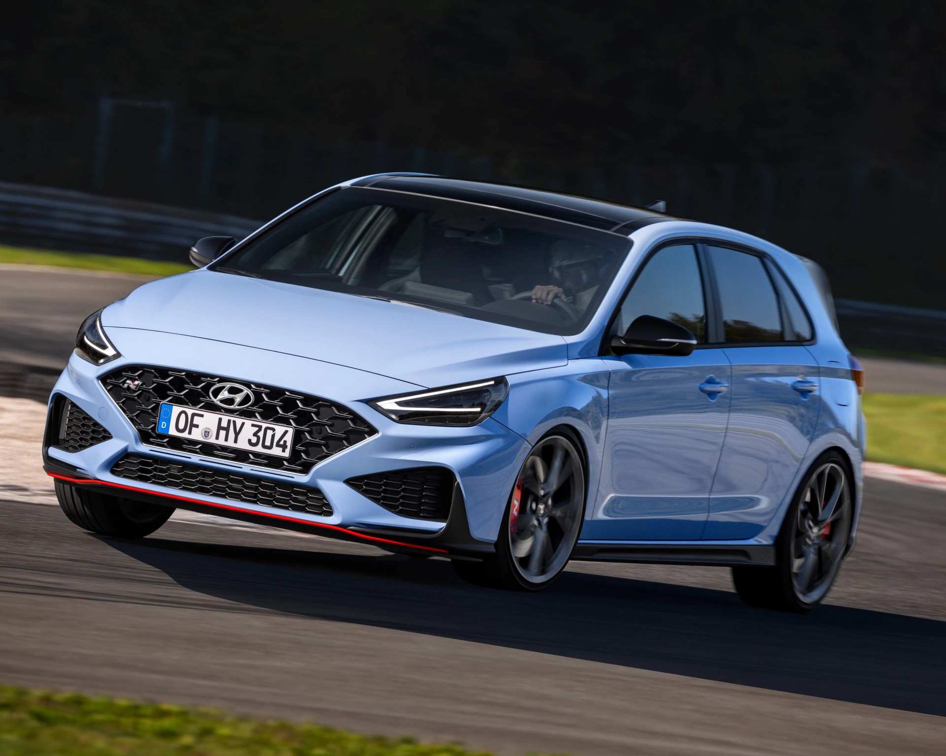 Light blue Hyundai hatchback with black roof and red trim cornering on a racetrack.