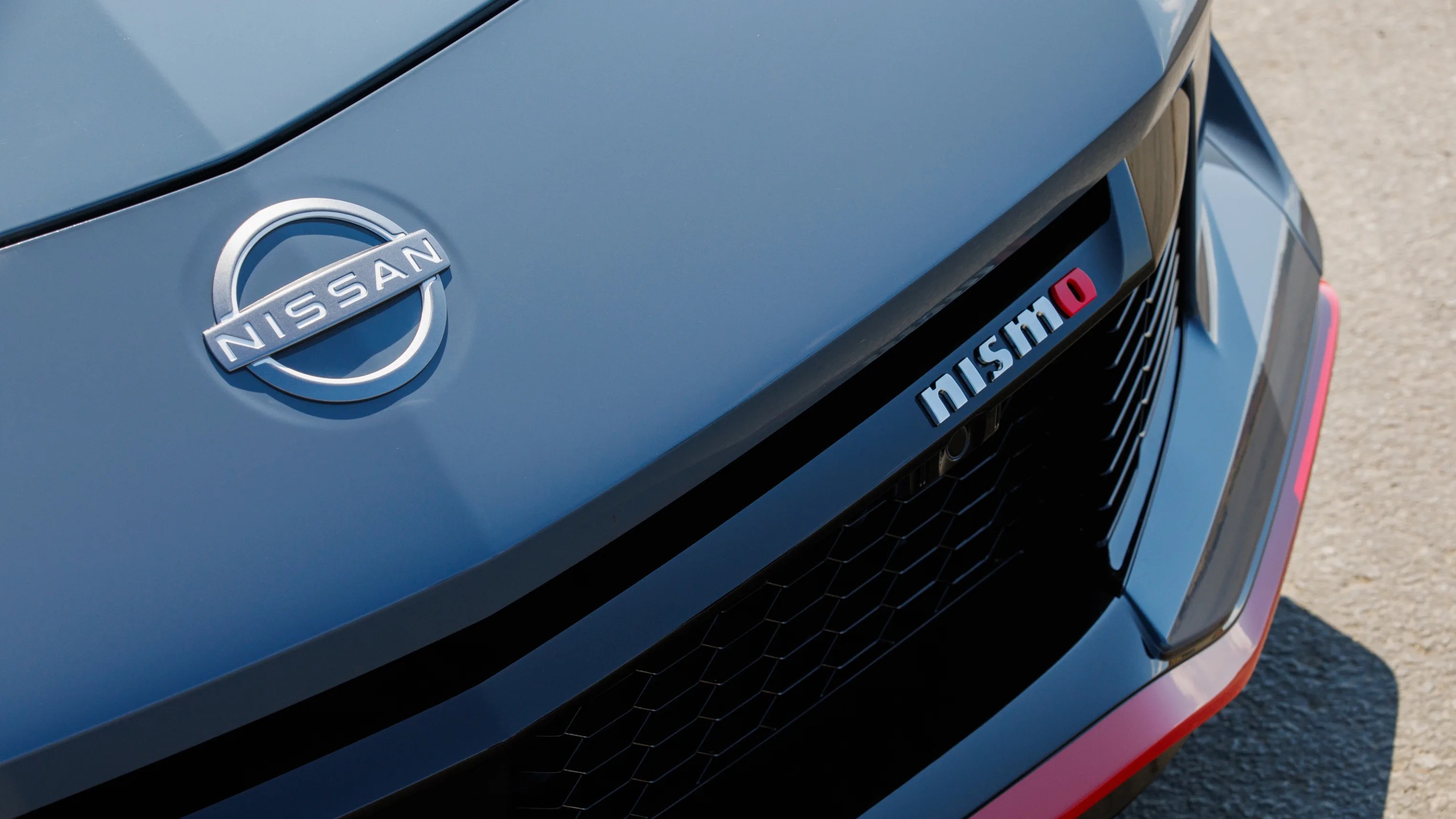 Front grille of a blue Nissan car with a silver Nissan emblem and a "nismo" badge.