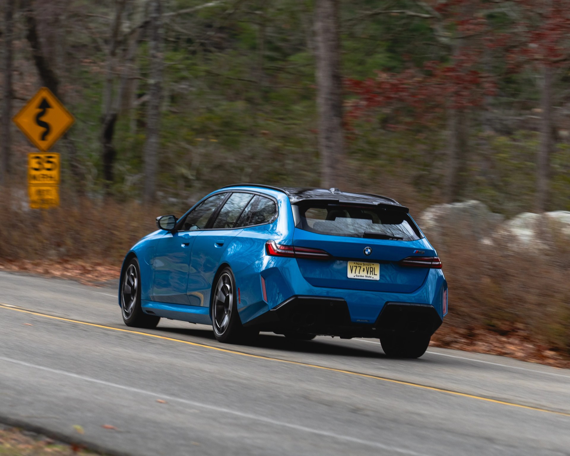 Blue BMW M3 Touring driving on a winding road with a 35 mph speed limit sign visible.