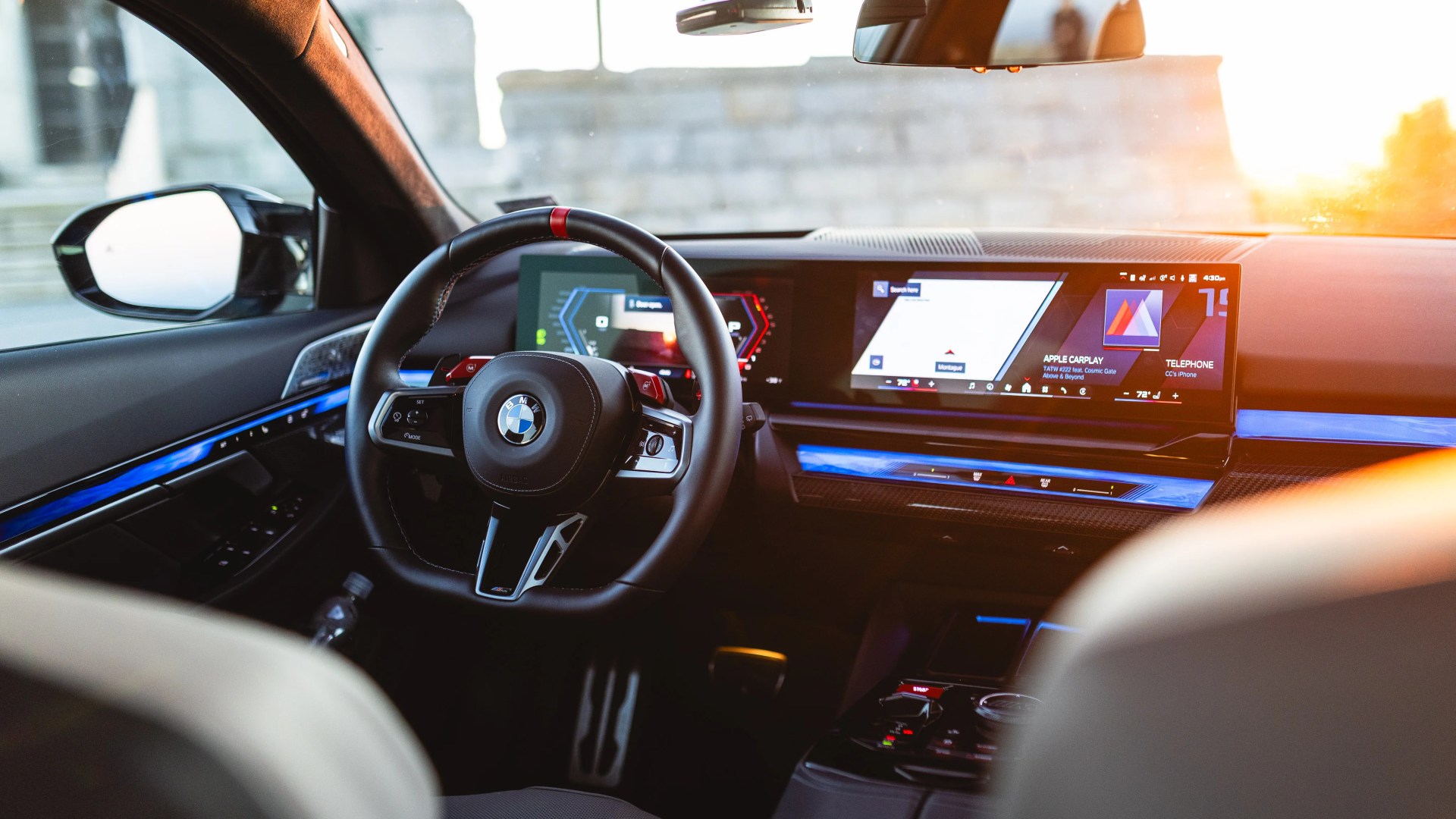 Interior view of a BMW car showing a black leather steering wheel with red accents and a digital dashboard with navigation display.