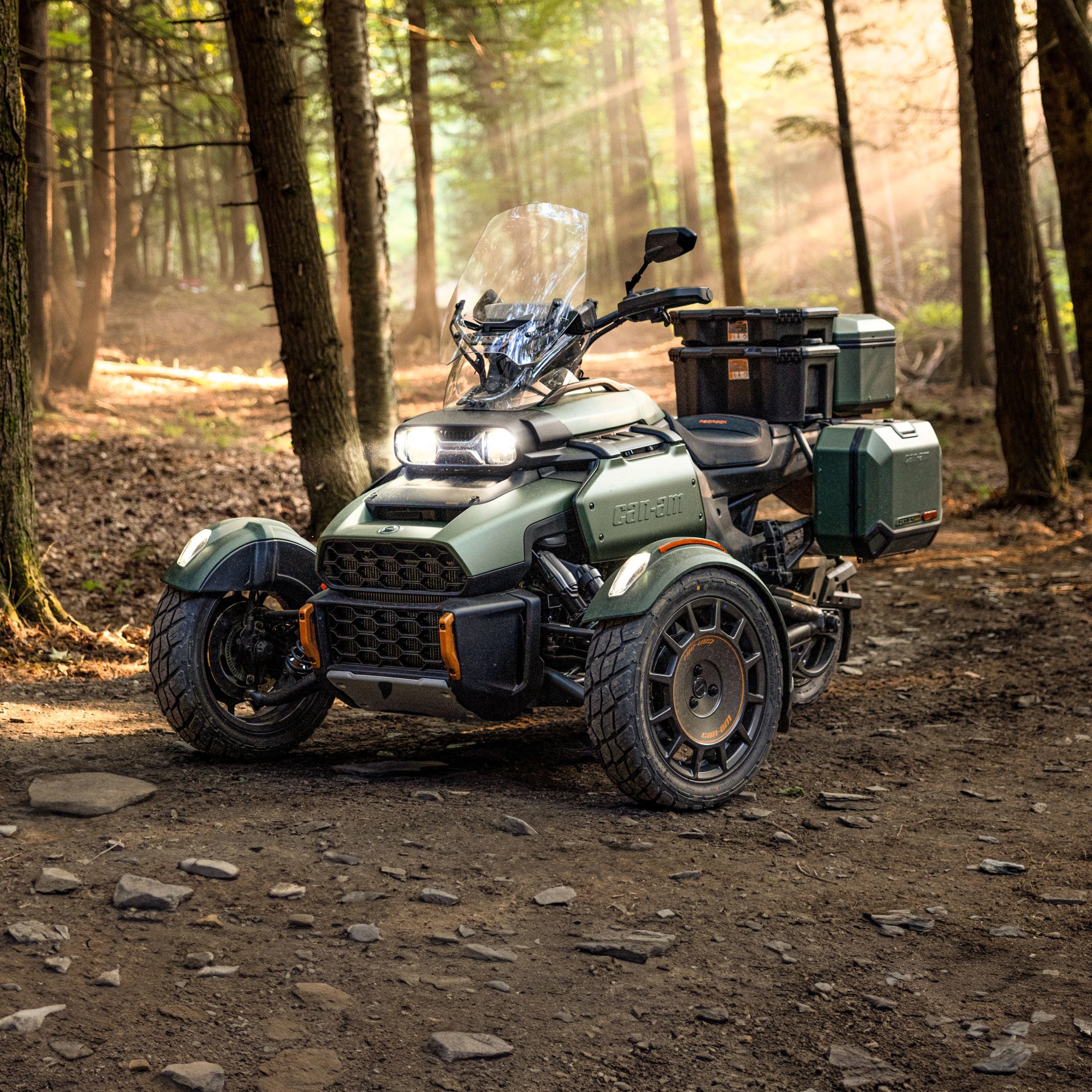 Green Can-Am three-wheeled motorcycle with storage boxes parked on a forest trail.