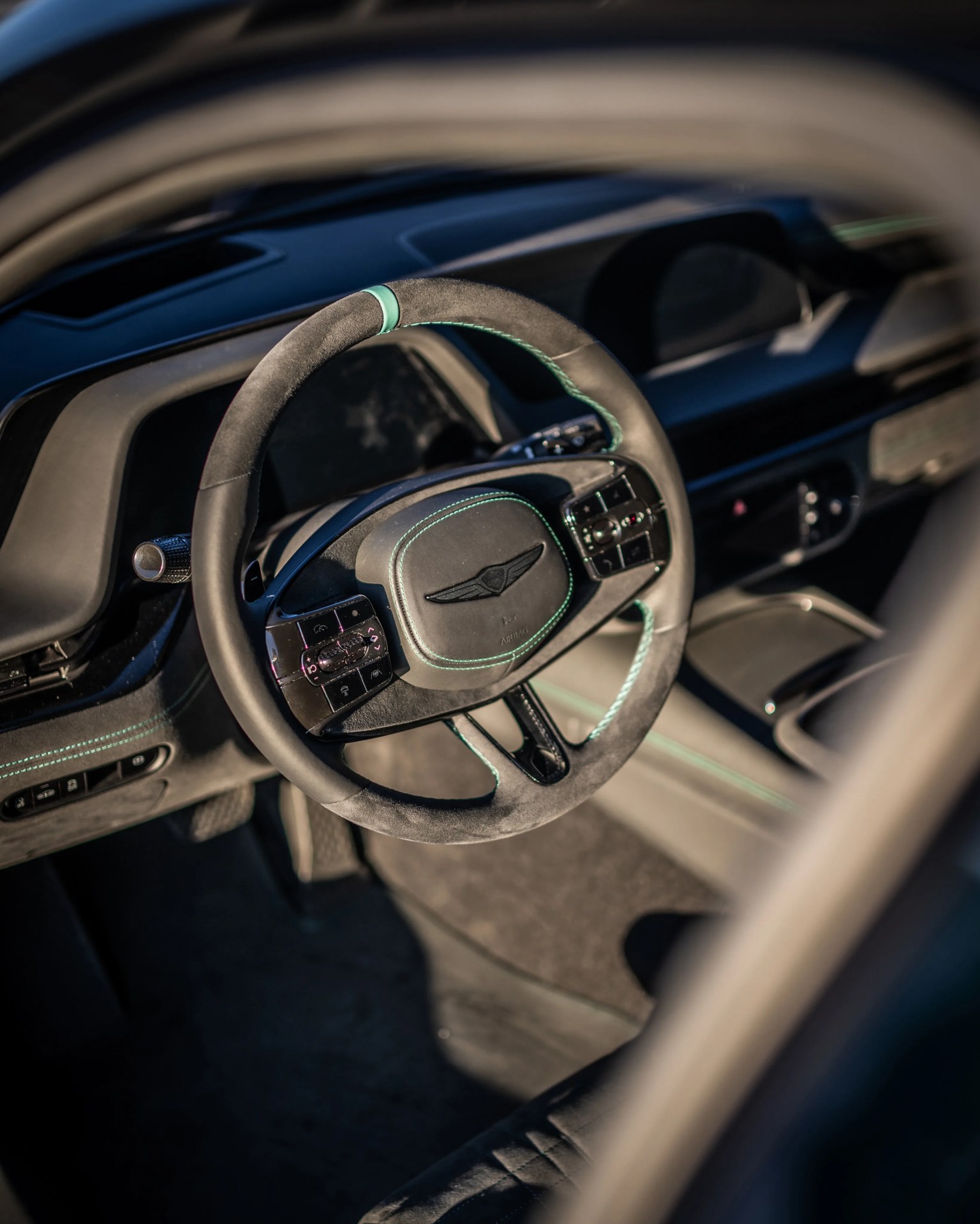 Black suede steering wheel with turquoise stitching and control buttons inside a luxury car.
