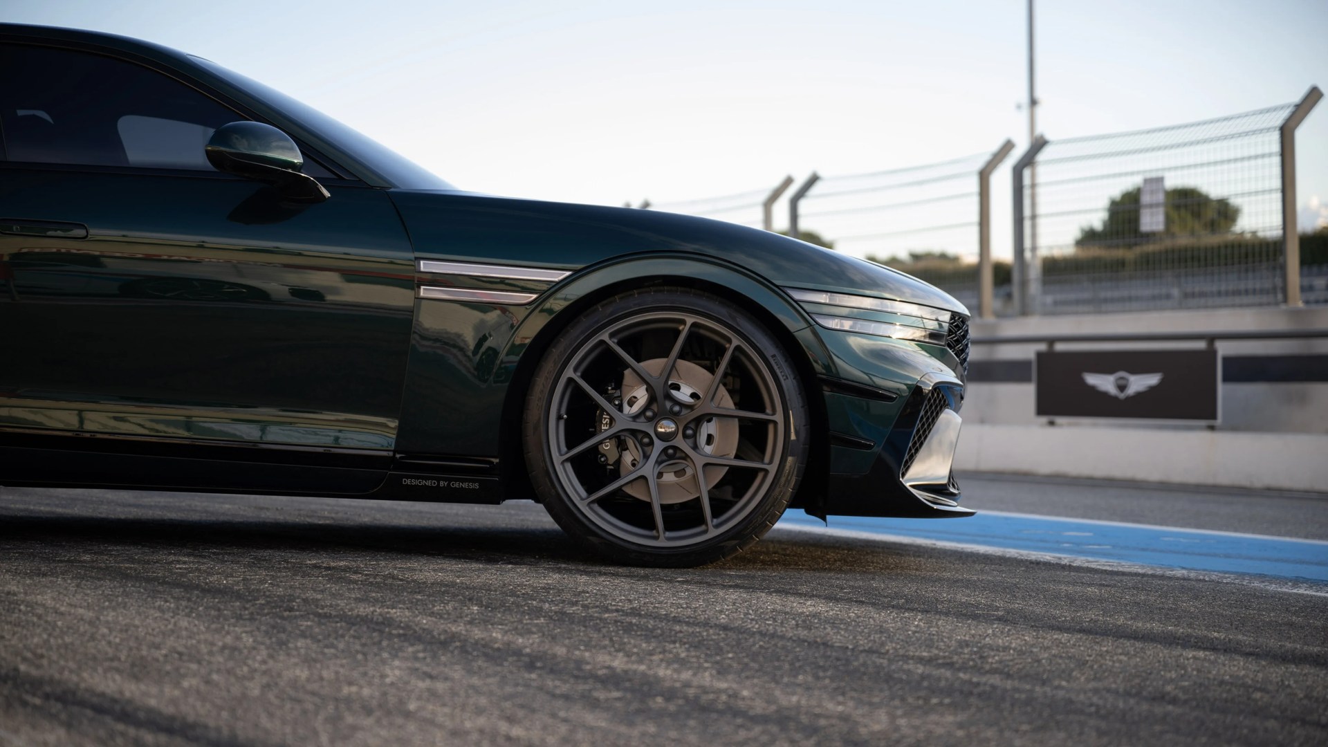 Front side view of a dark green Genesis car with black alloy wheel on a race track.