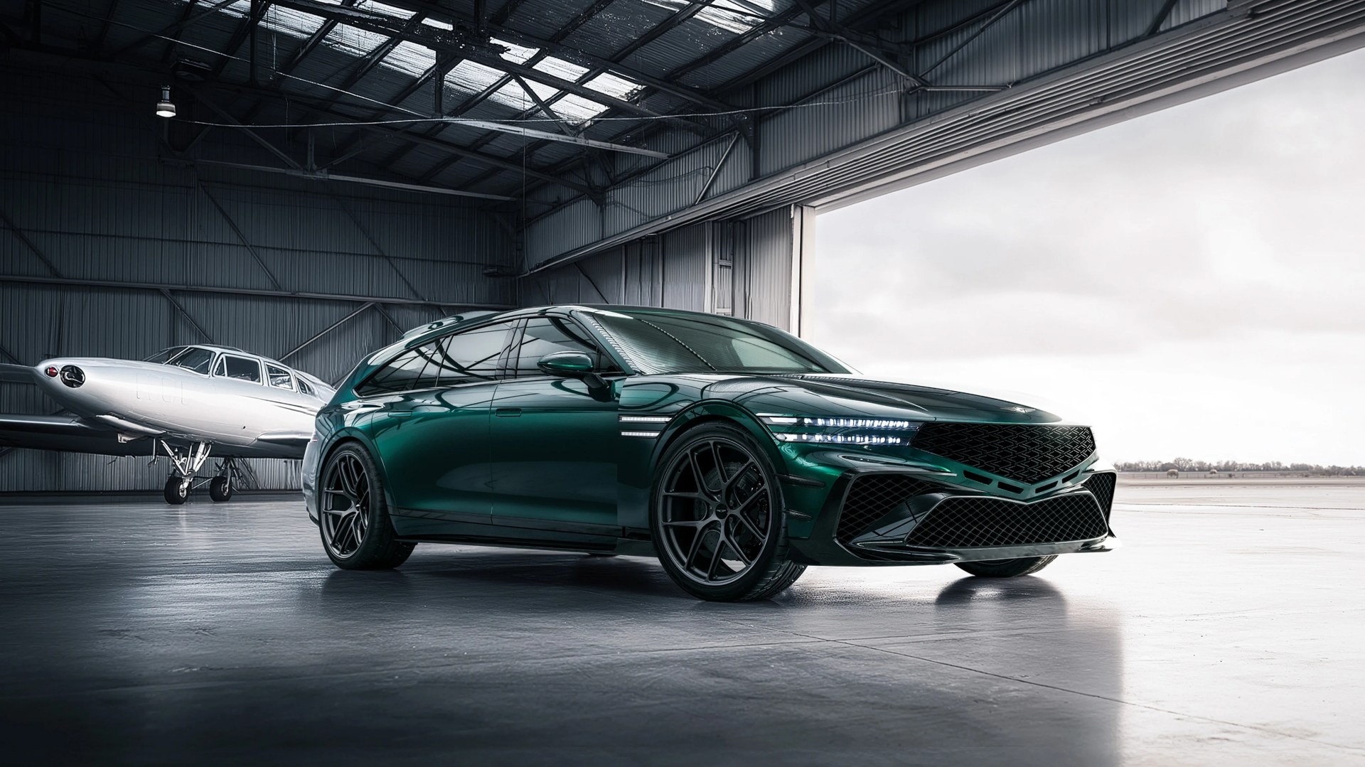Dark green luxury station wagon with black wheels parked inside an aircraft hangar near a small white airplane.
