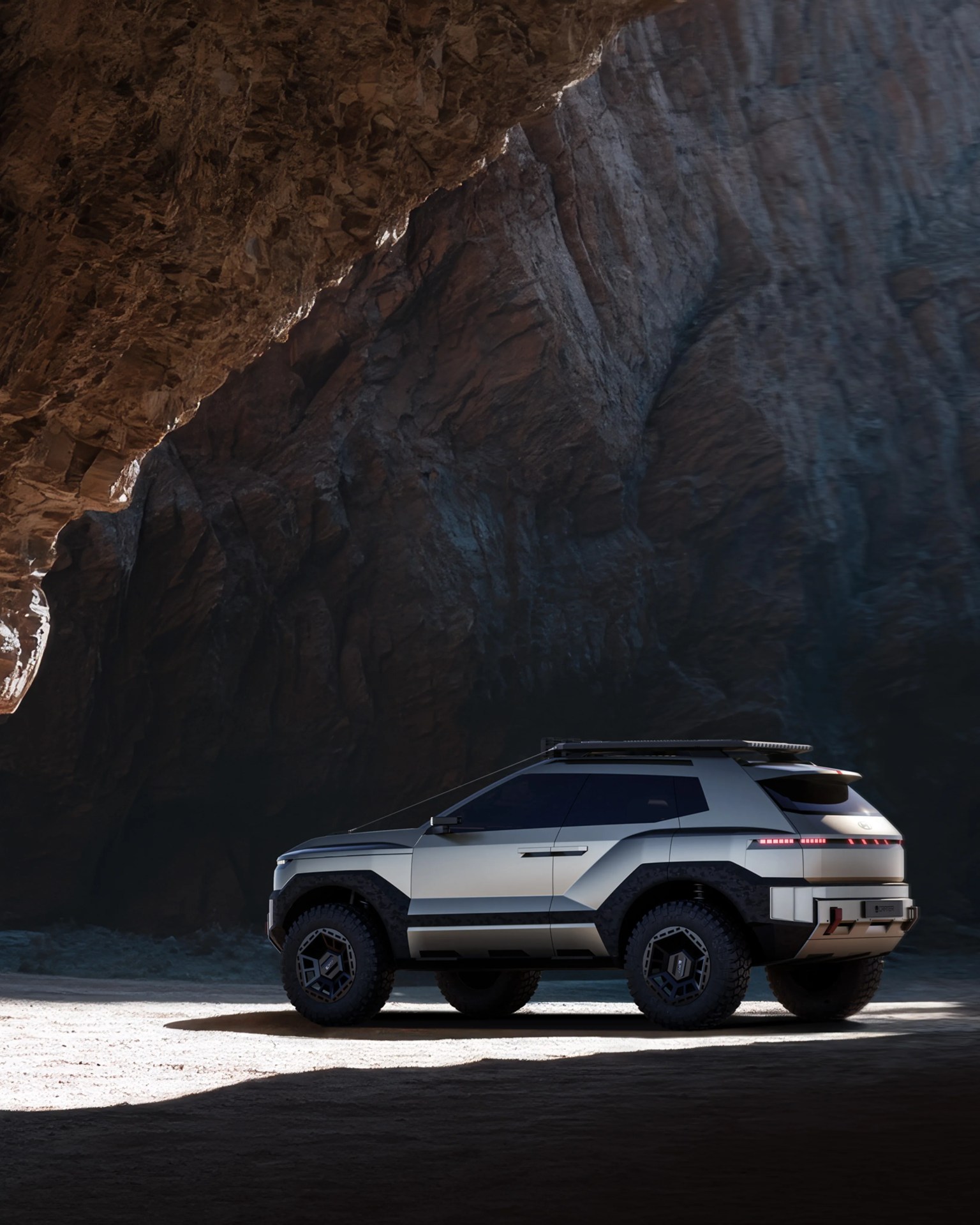 Silver futuristic SUV with black accents and off-road tires parked inside a rocky cave.