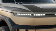 Front close-up of a matte tan vehicle hood with digital-style LED headlights and black pixelated fender flares.