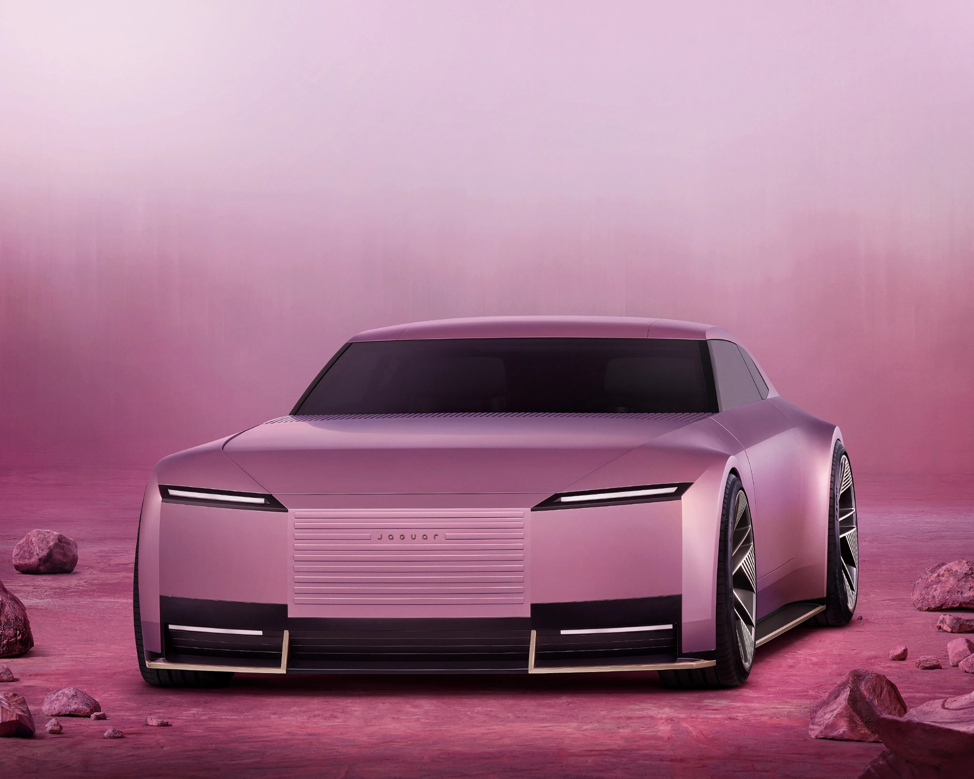 Matte pink futuristic Jaguar concept car with sleek LED headlights on a pink rocky surface.