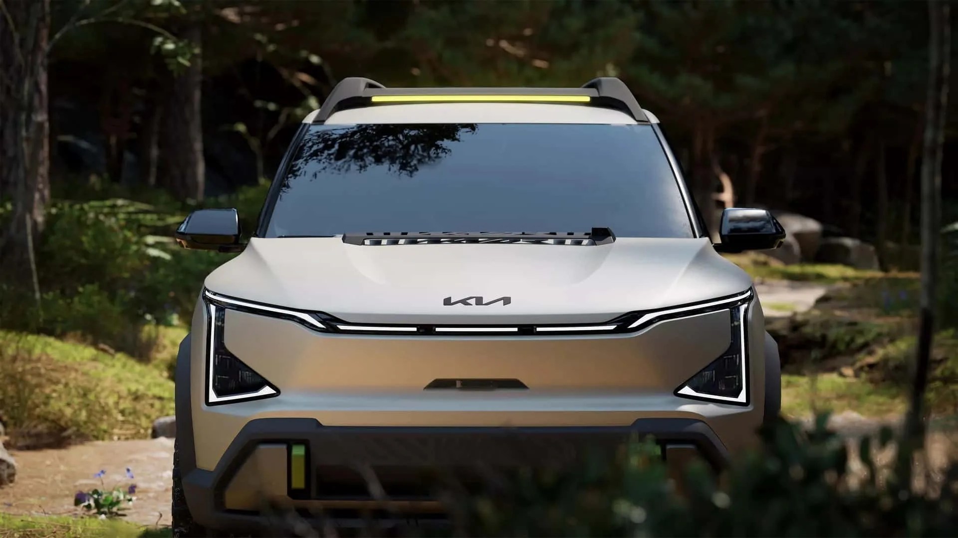 Front view of a silver Kia SUV with sleek LED headlights and a yellow light bar on the roof, set in a forest background.