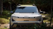 Front view of a silver Kia SUV with sleek LED headlights and a yellow light bar on the roof, set in a forest background.
