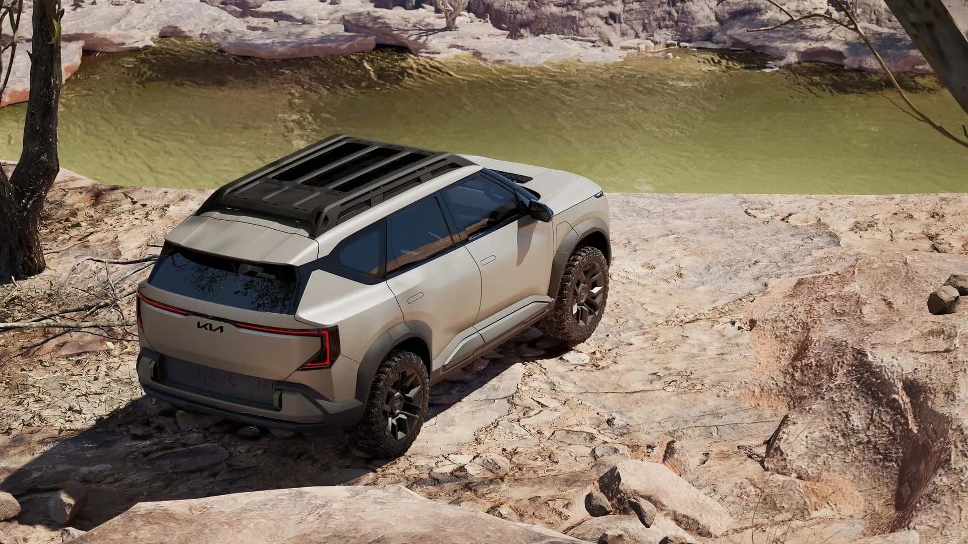 Beige Kia SUV with black roof rack parked on rocky terrain near a greenish river.
