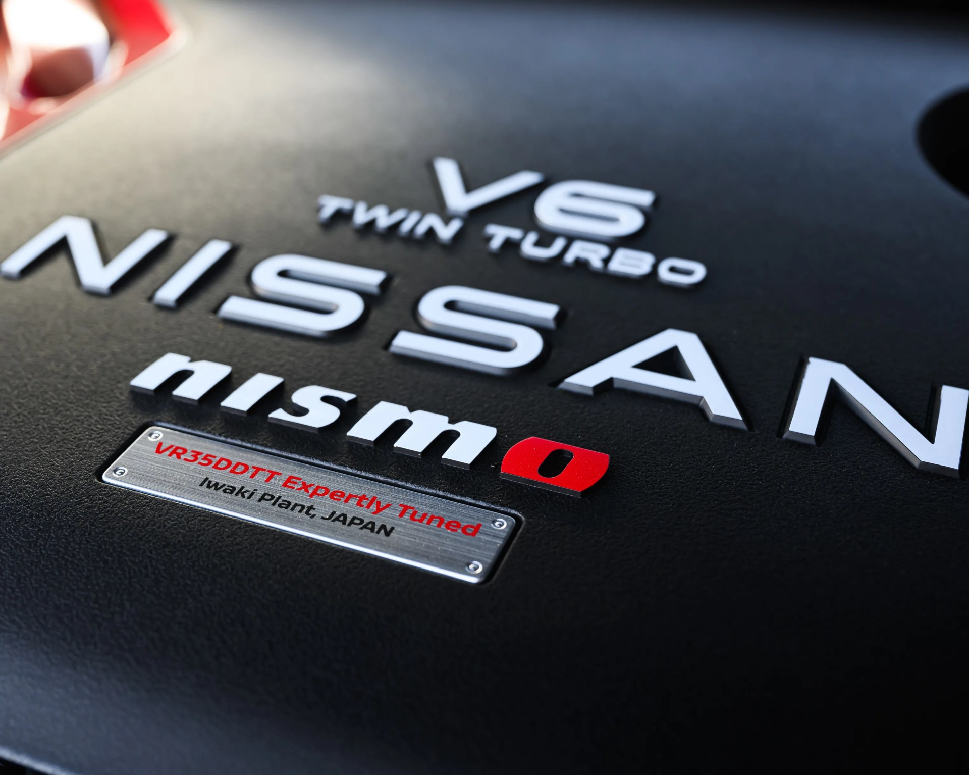 Close-up of a black Nissan V6 Twin Turbo engine cover with white "nismo" and a metal plate reading "VR35DDTT Expertly Tuned Iwaki Plant JAPAN.