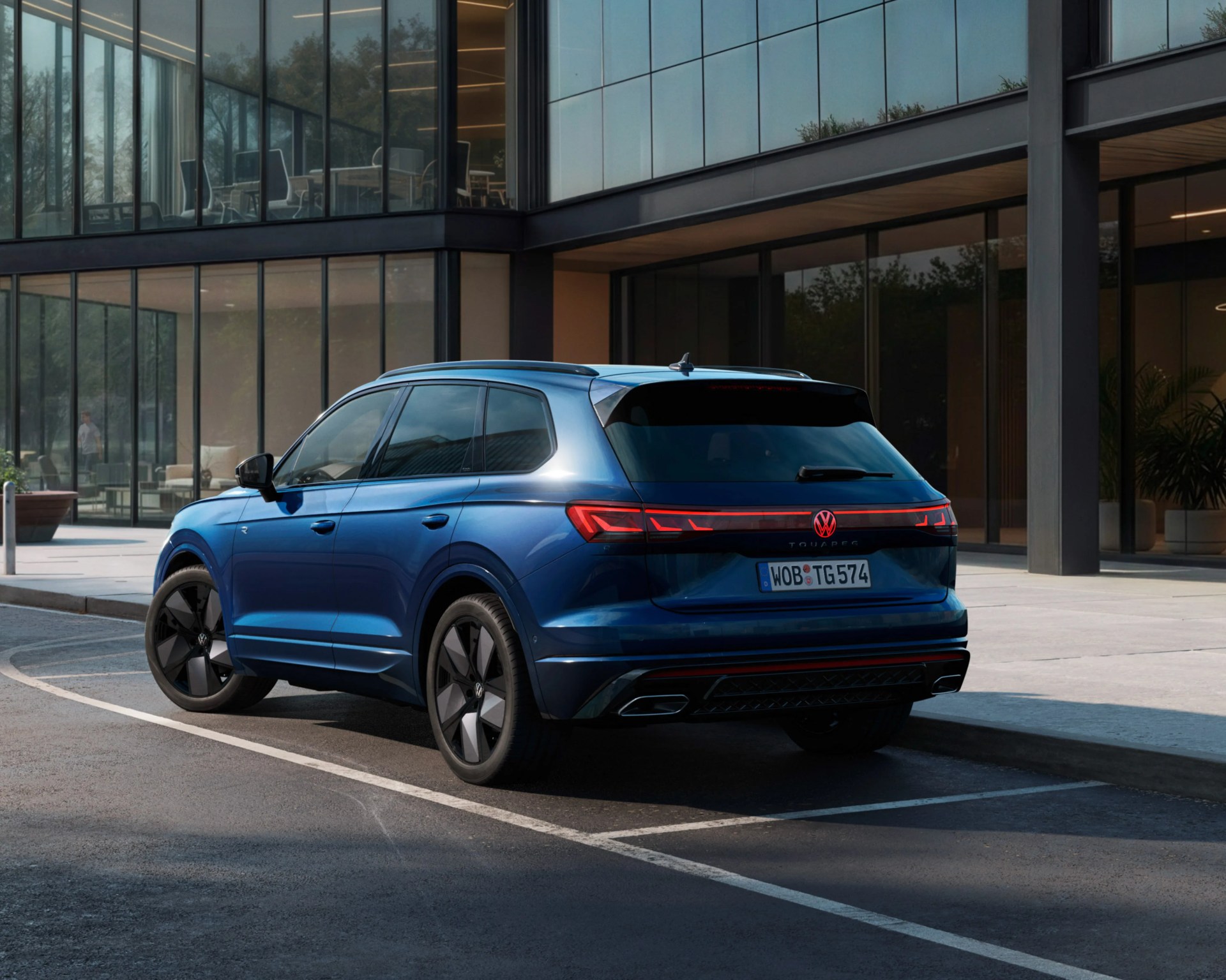 Blue Volkswagen Touareg SUV parked in front of a modern glass building.