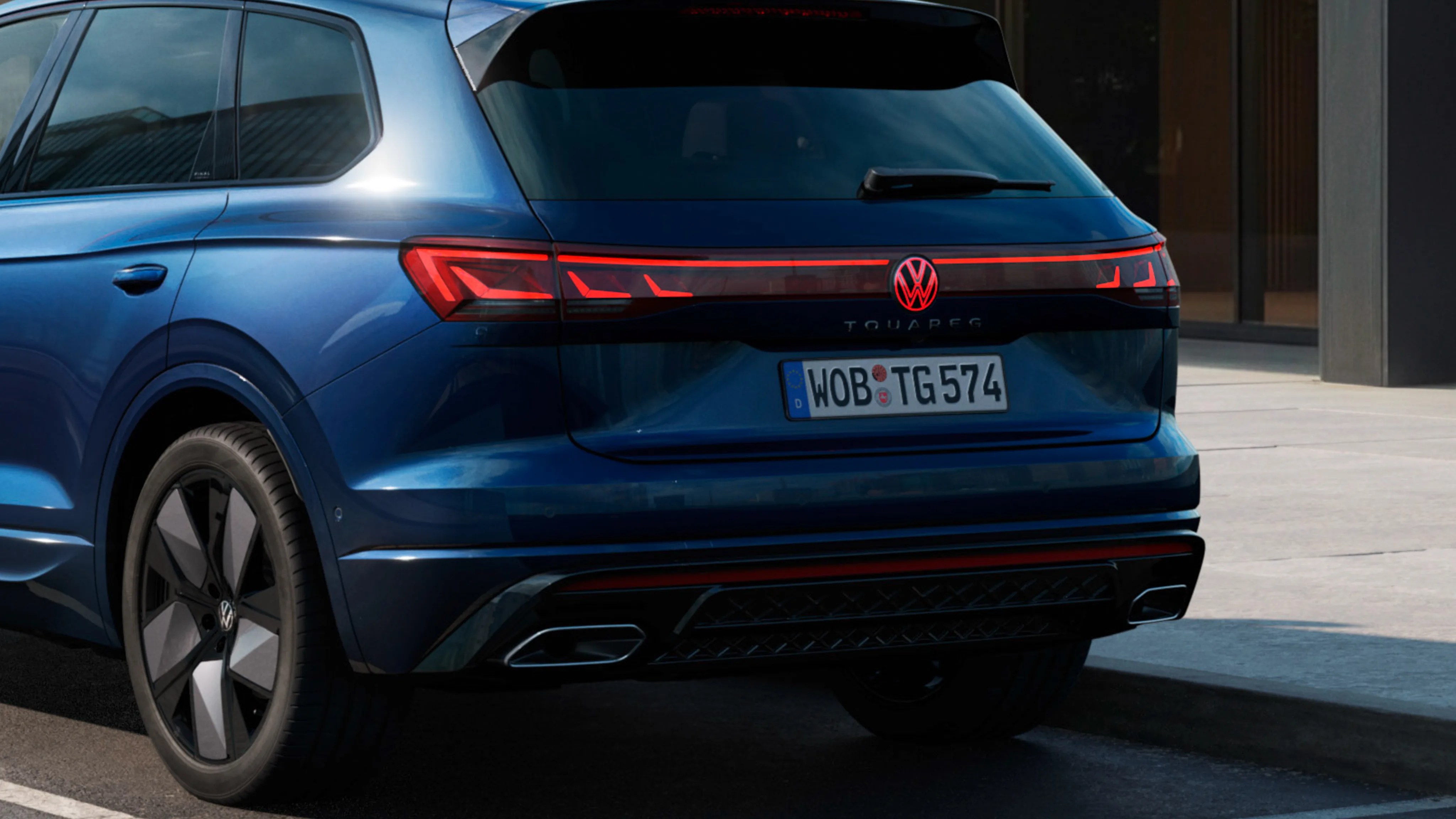 Rear view of a blue Volkswagen Touareg SUV with illuminated taillights and black alloy wheels parked on a street.
