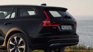 Rear side view of a black Volvo V60 Cross Country with illuminated taillights near a body of water.