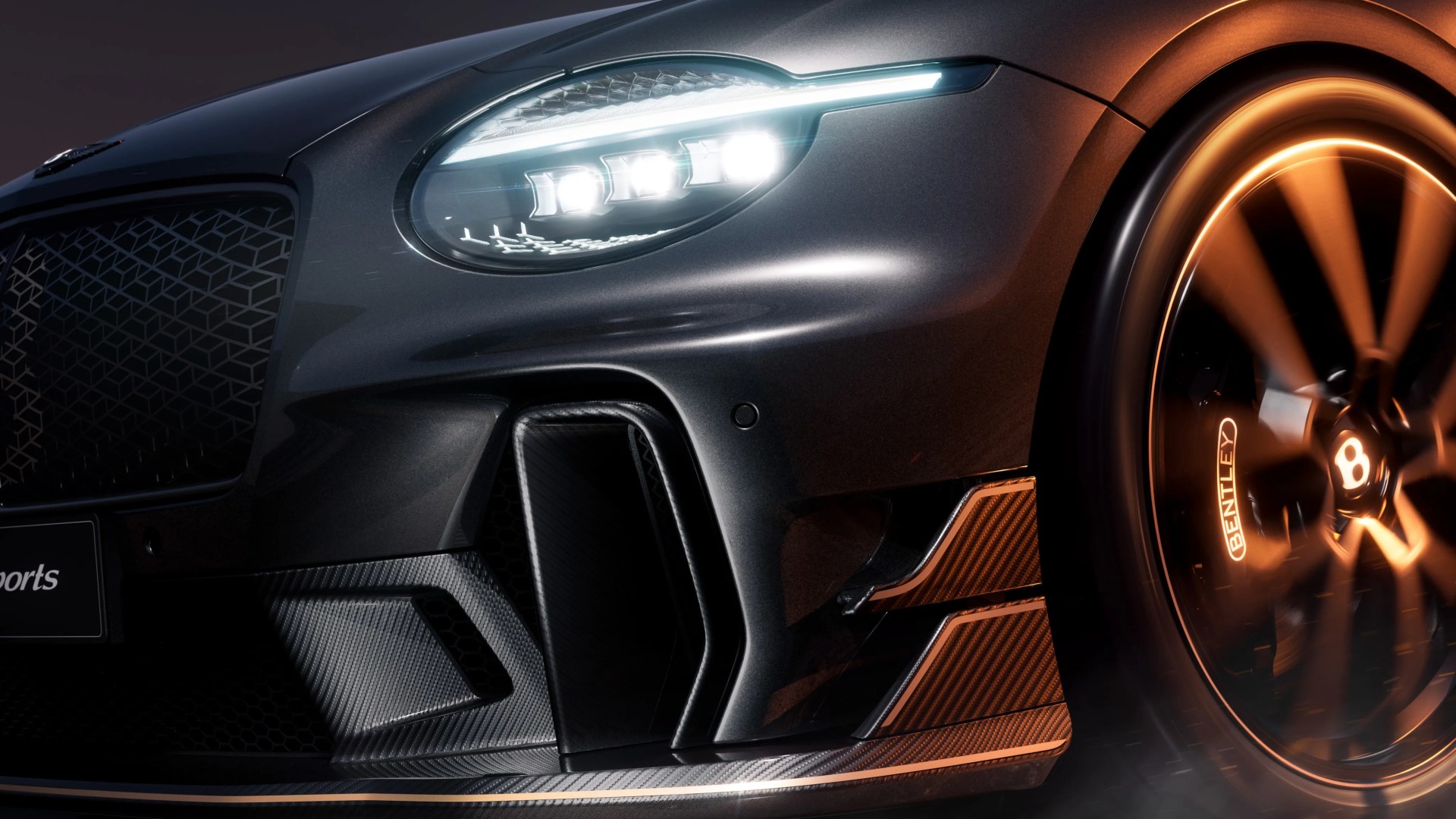 Close-up of a dark gray Bentley car front with illuminated LED headlight and spinning wheel with Bentley brake caliper.