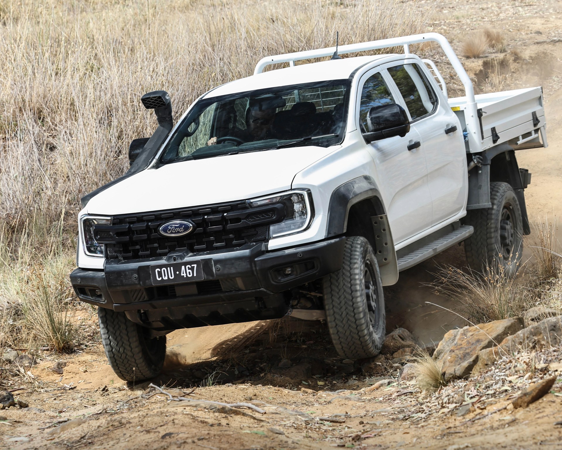 White Ford pickup truck with black grille and snorkel driving off-road on a dirt trail.