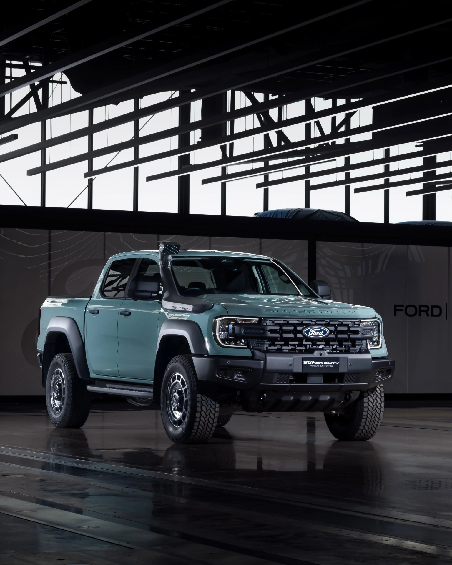 Light blue Ford Super Duty pickup truck prototype with off-road tires and snorkel in an industrial setting.