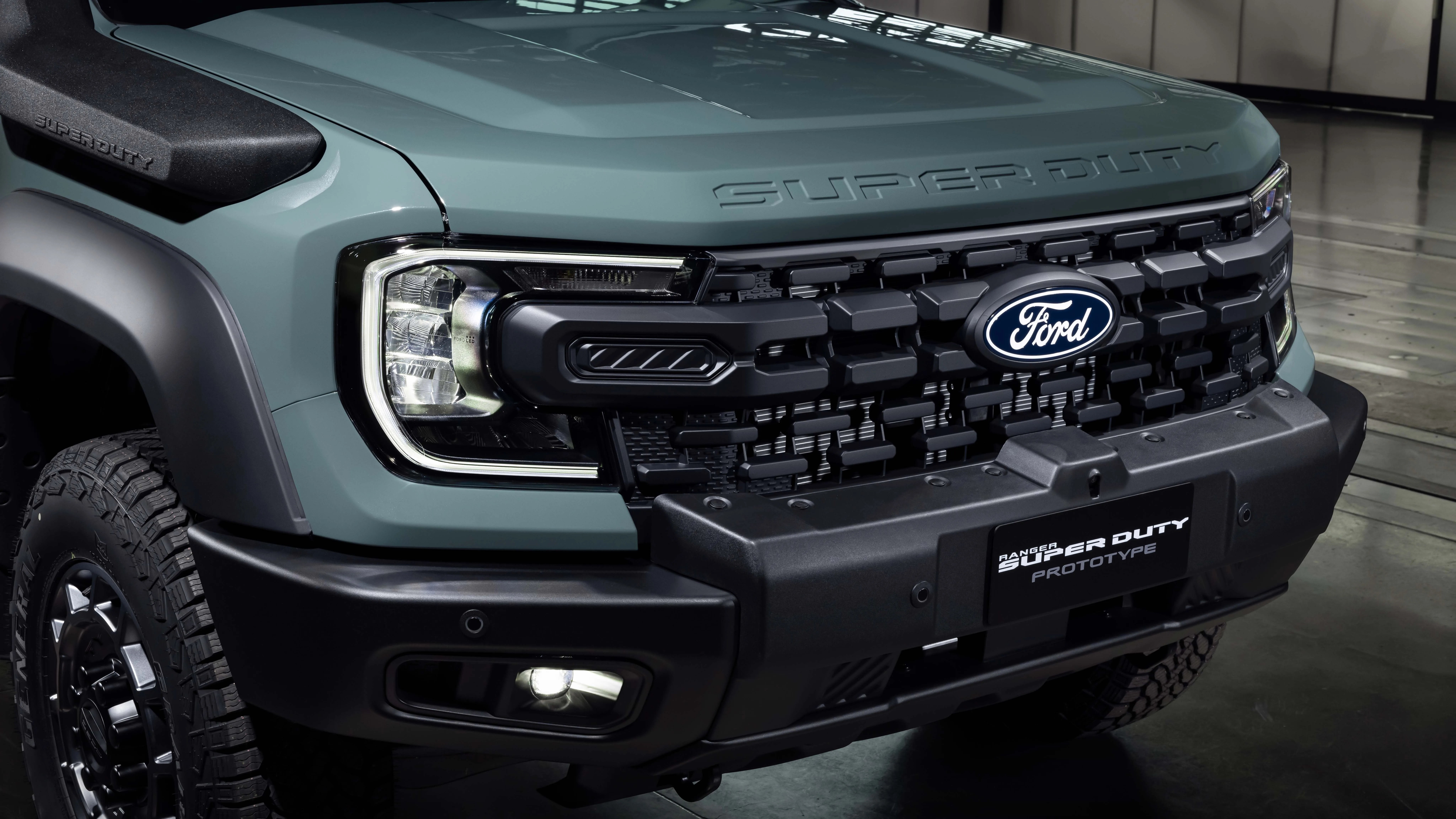 Front grille and headlight of a green Ford Ranger Super Duty prototype truck.