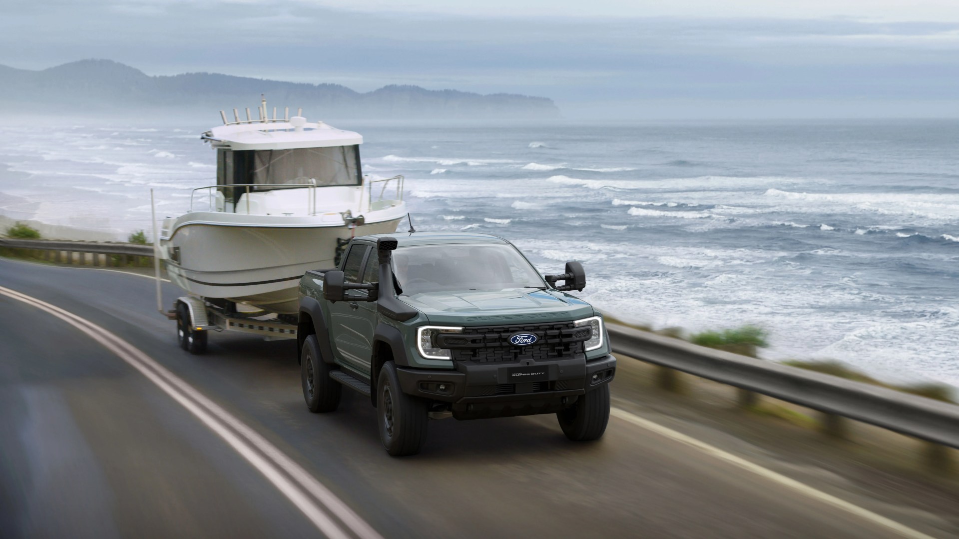 Green Ford Super Duty pickup truck towing a white boat on a coastal road with ocean waves in the background.